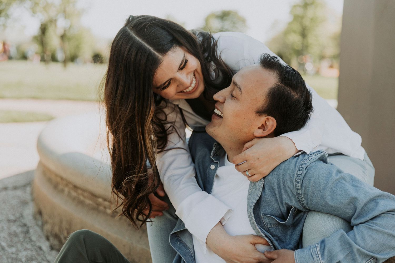 Saul and Lauren sit on a water fountain as they laugh and look into each other's eyes