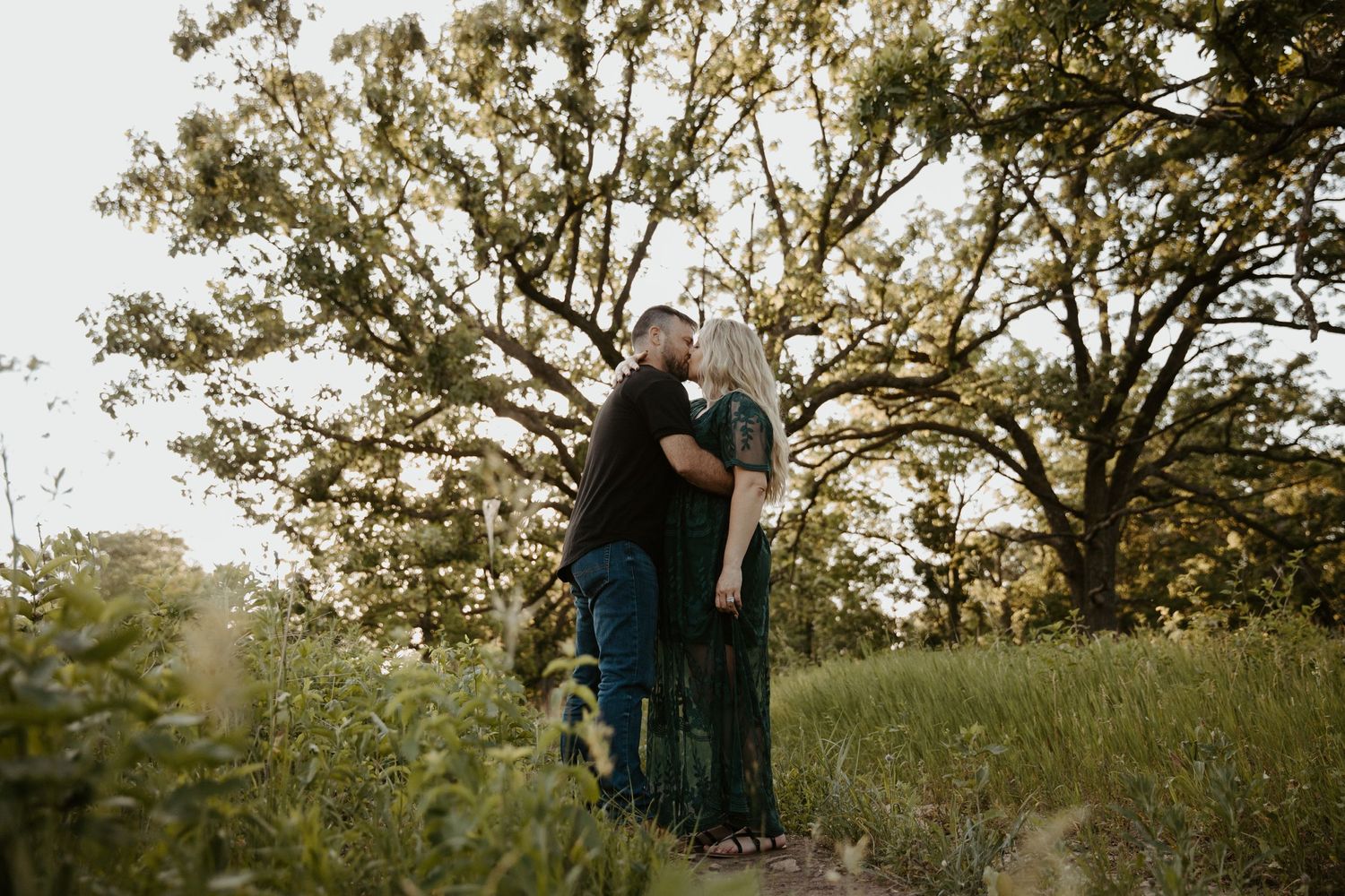 engaged couple kissing passionately in front of a large tree