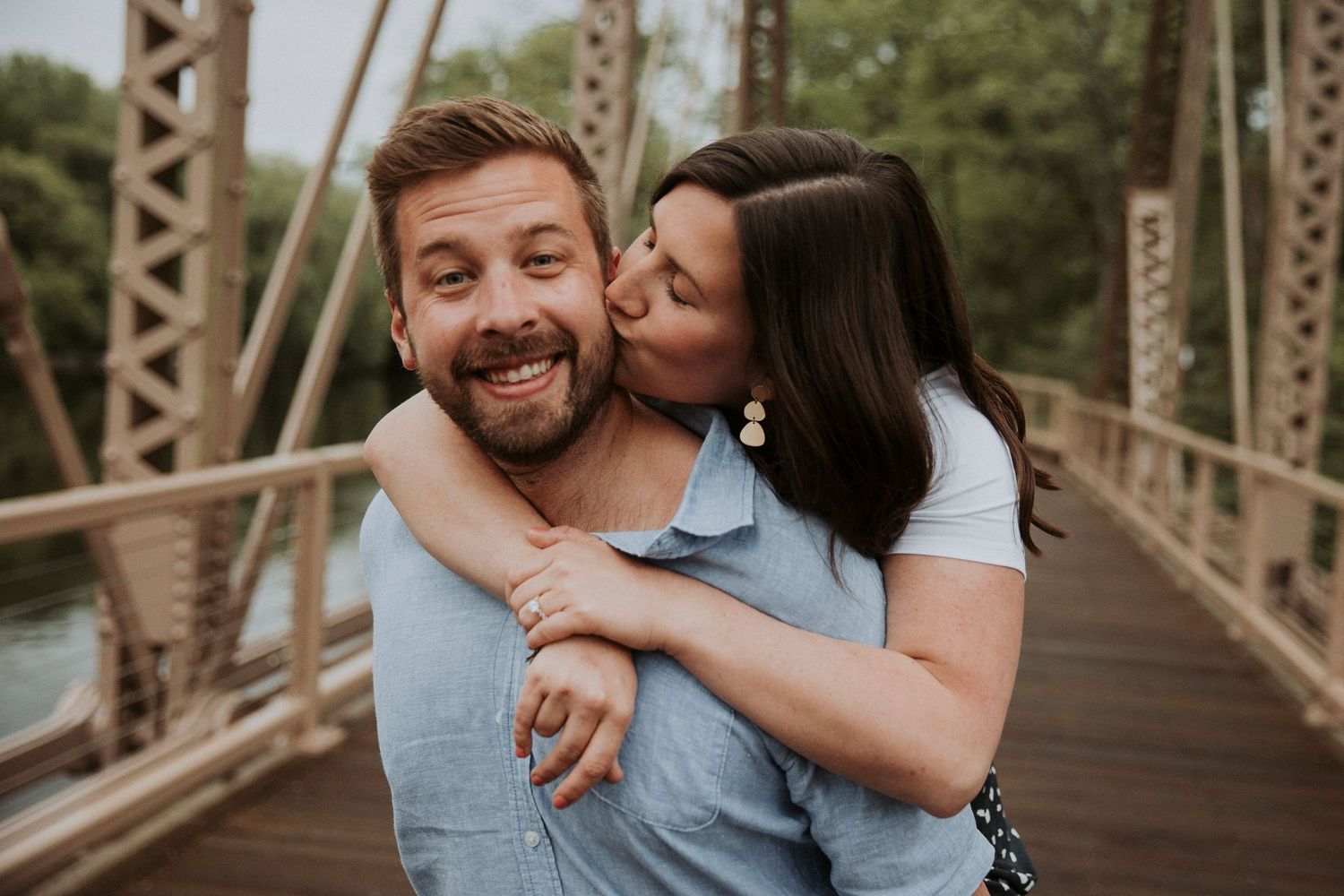 woman kisses her fiance on the cheek on a bridge