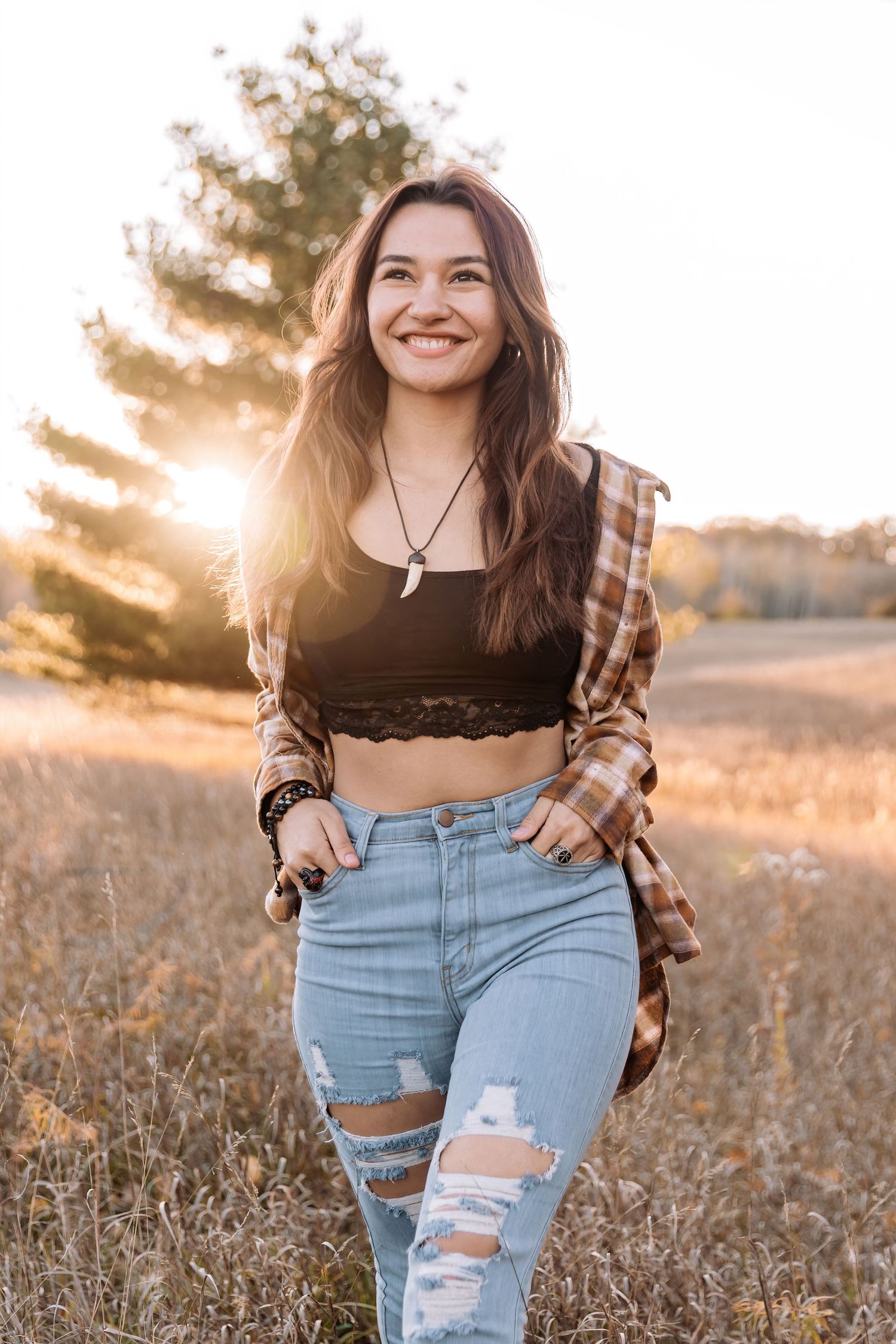 Tasia walks with her hands in her pockets away from a golden sunset in a tall grassy field at Ritter Farm Park