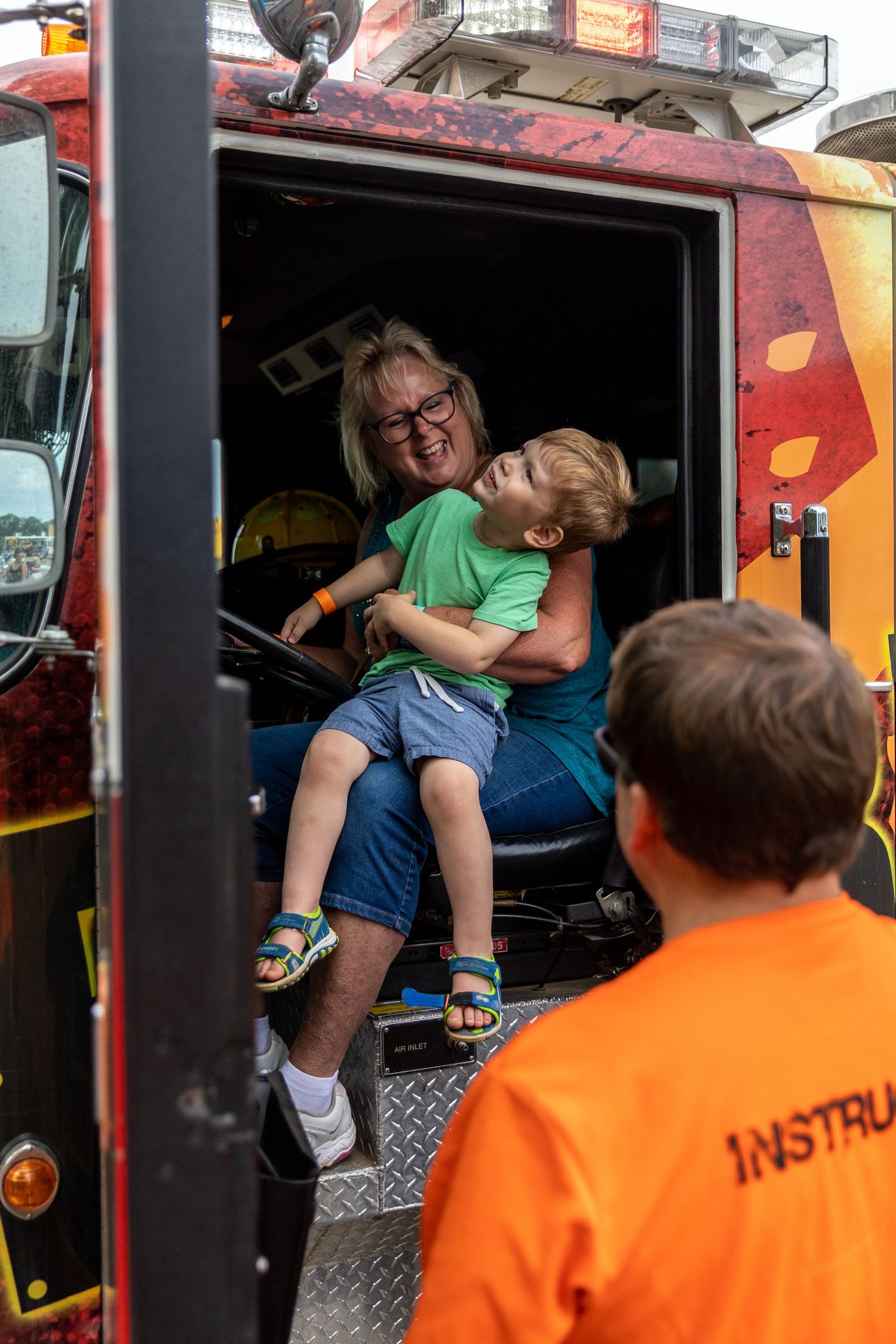 Mom and her son smile as they sit in the back seat of a fire truck
