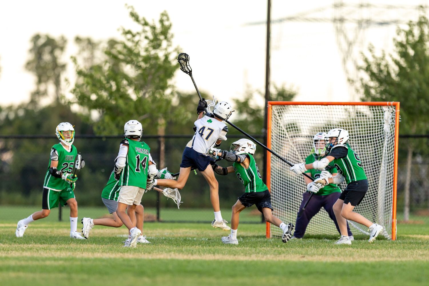 Youth lacrosse player jumps up to shoot over his defenders