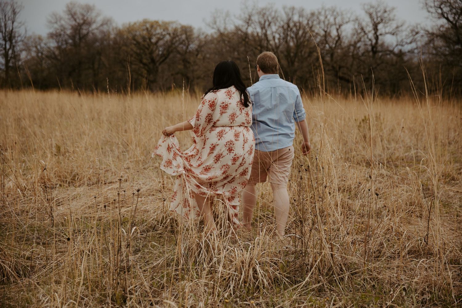 Engaged couple strolling through a tall grassy field