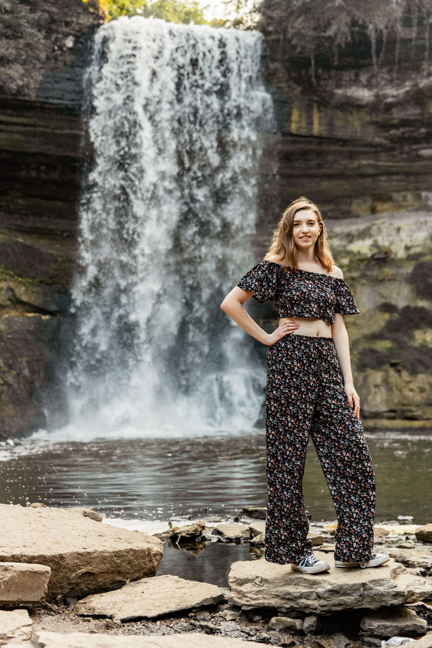 Teenager throws her hip out and her hand on her hip as Minnehaha Falls crashes down behind her