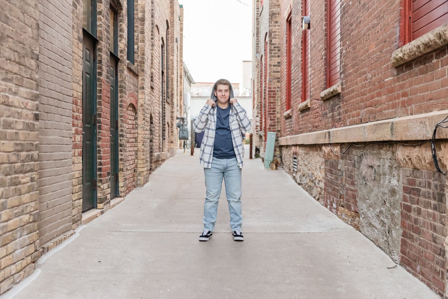 Erik pops his sweatshirt hood up in a brick and concrete covered alley