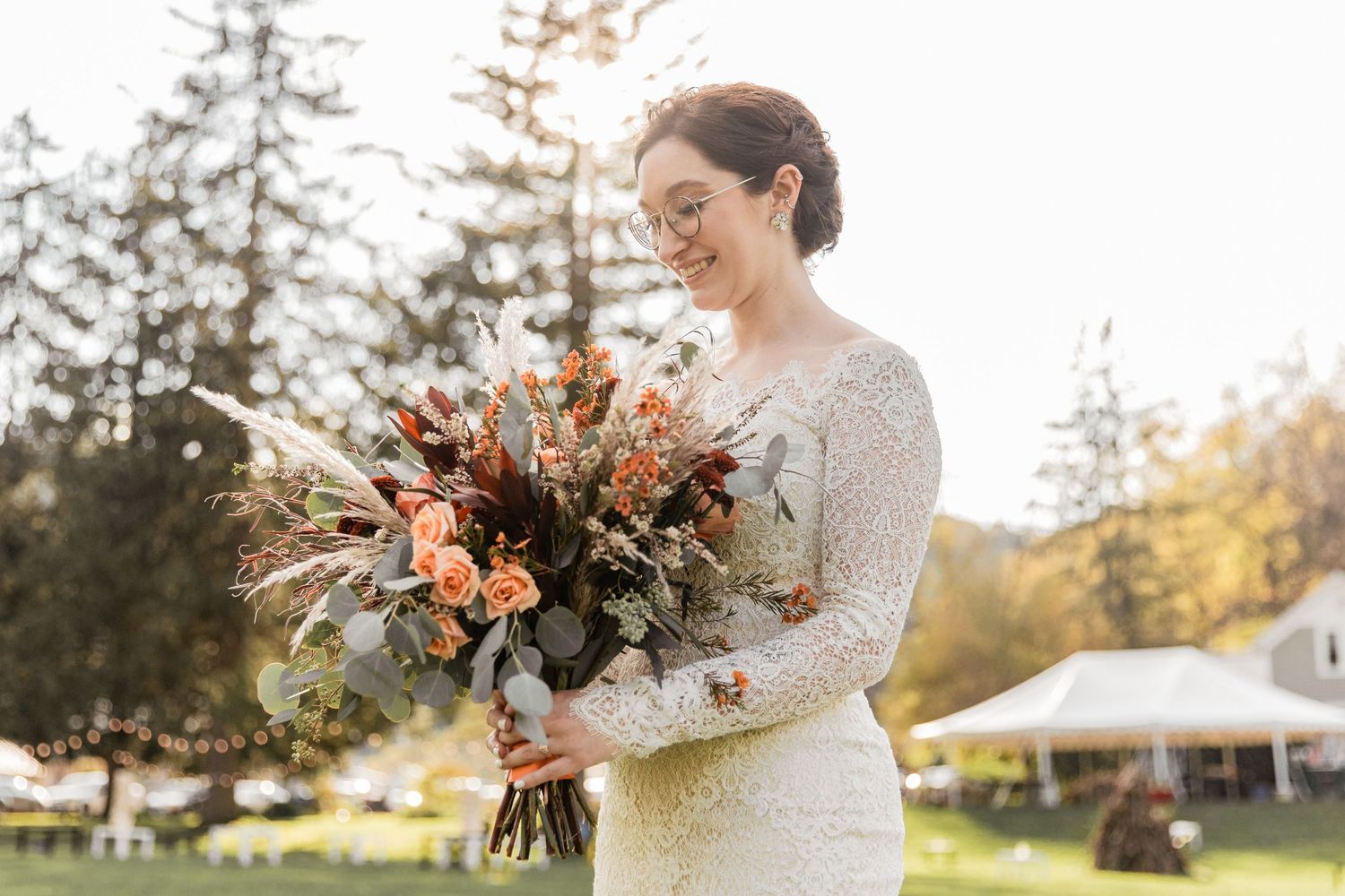 bride gazing into her autumn bouquet of flowers as sun sets behind her