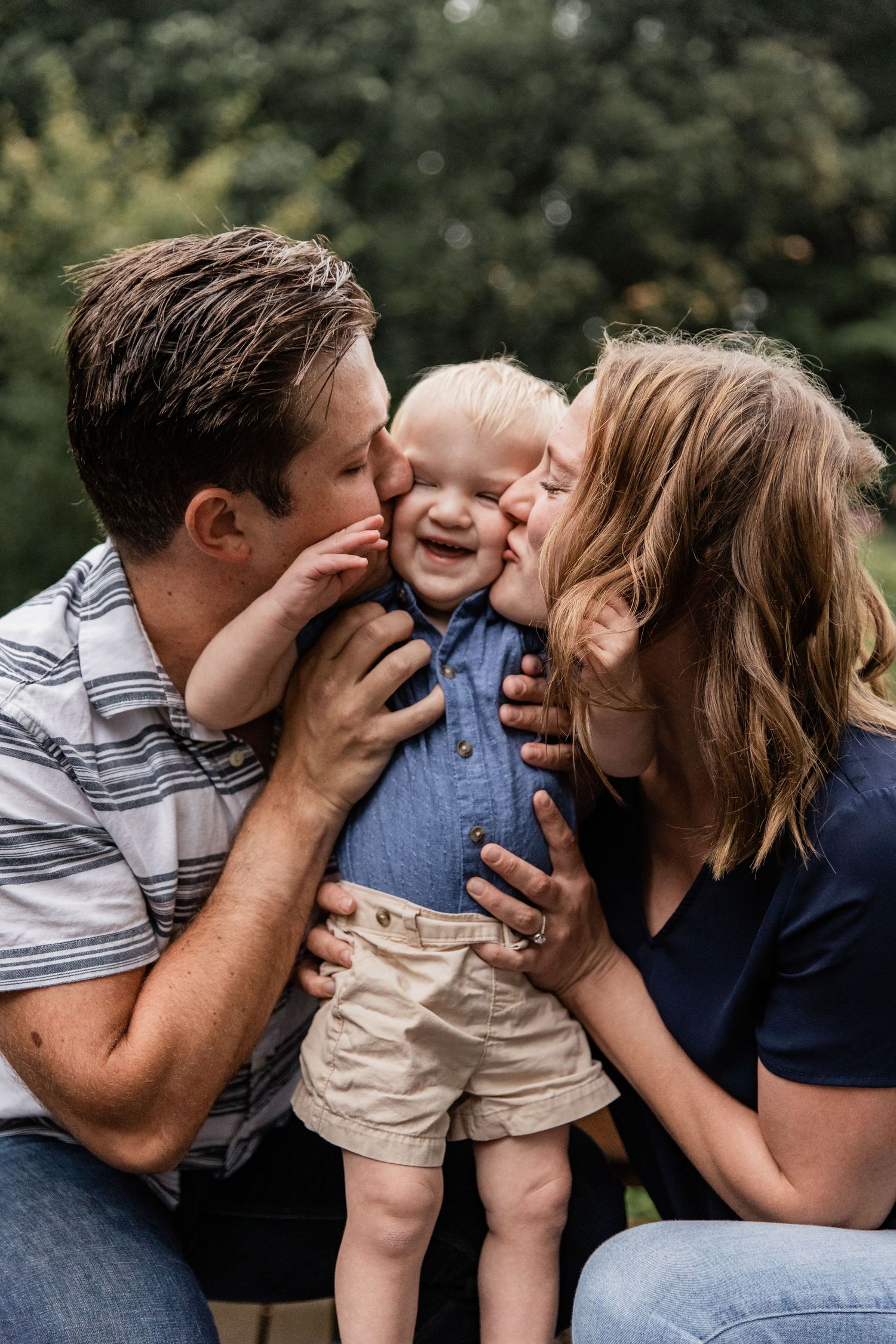Husband and wife kiss their toddler on his cheeks while he smiles