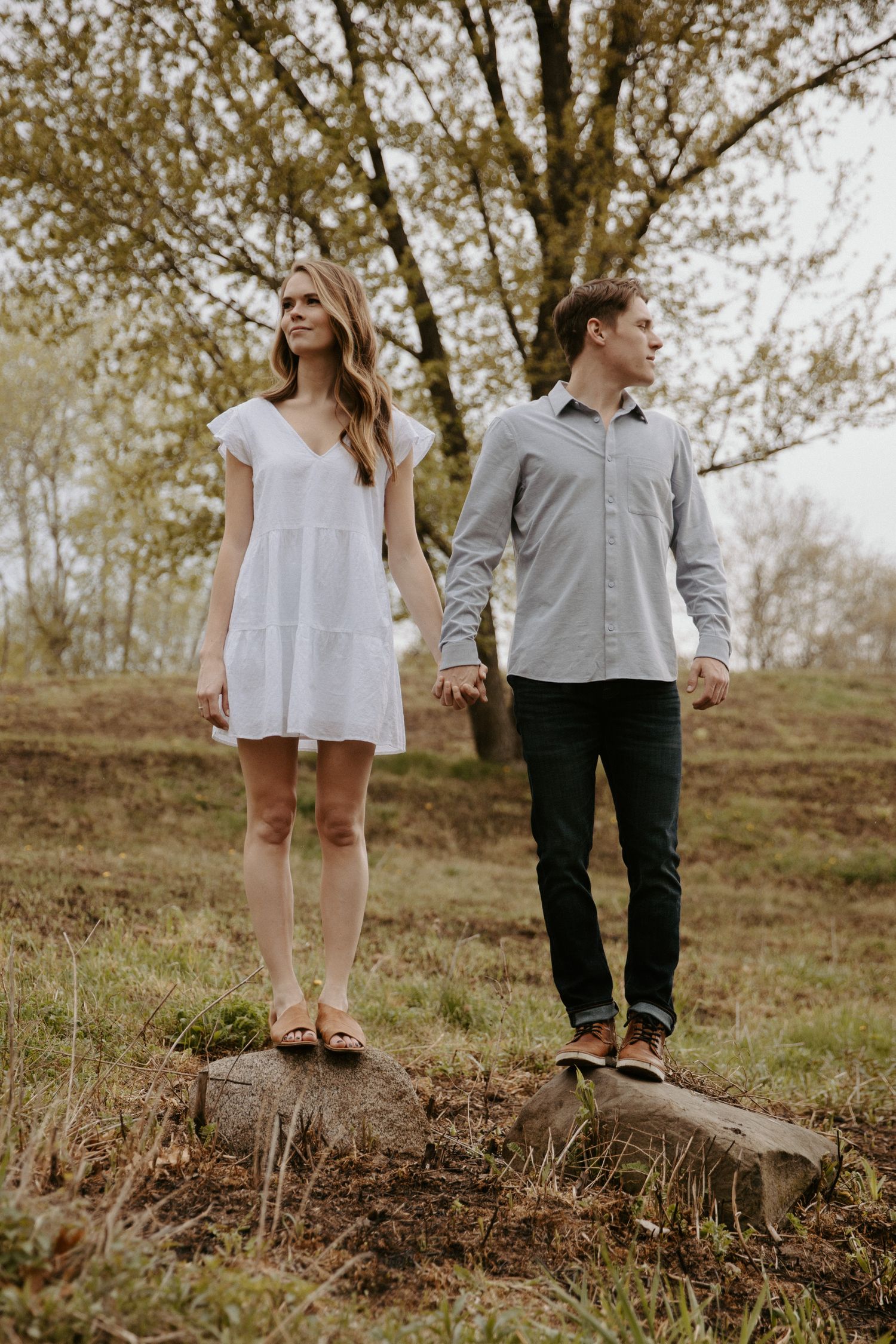 Young couple holds hands as they stare off into the distance standing atop a large tree stump