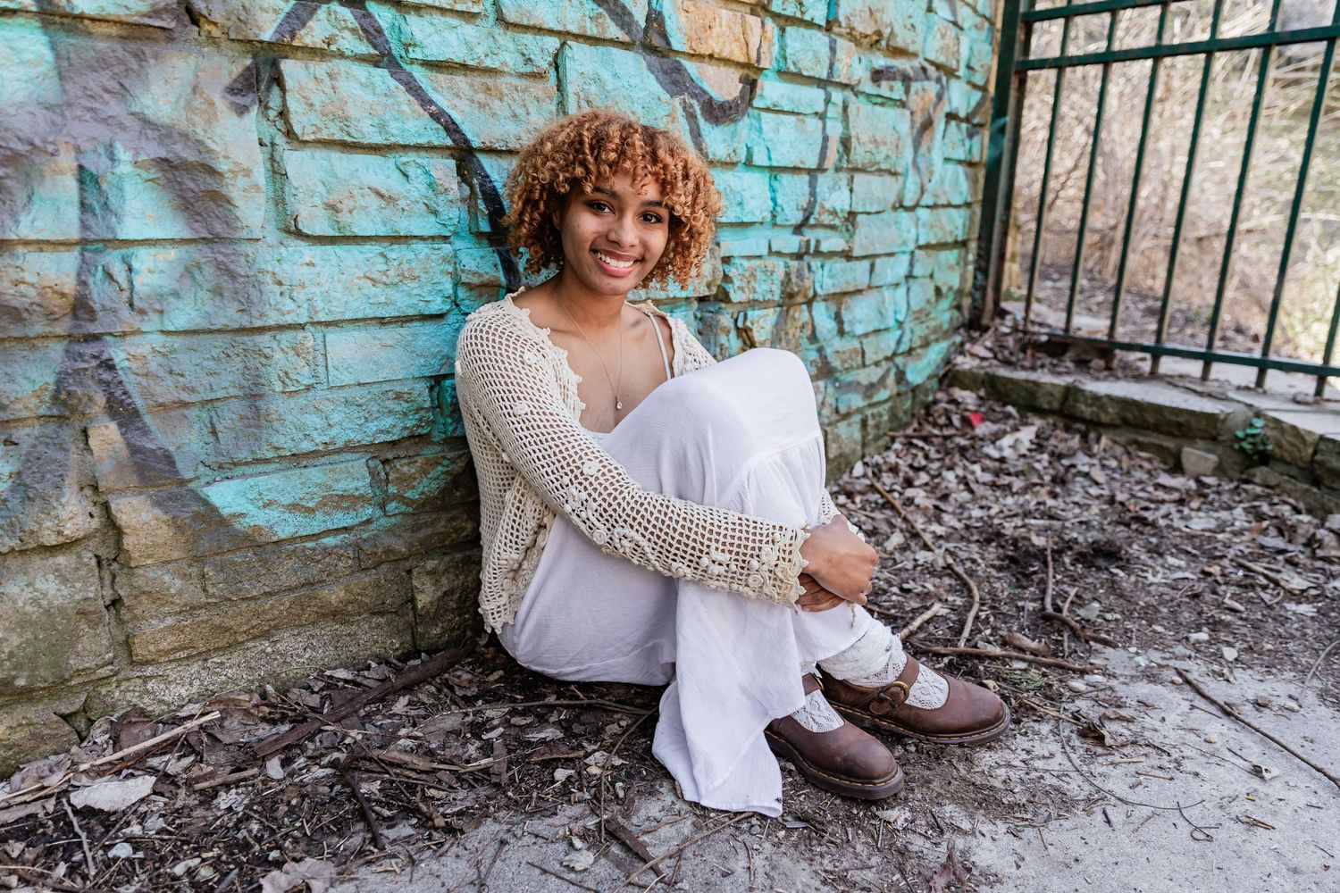 Young African American teen sits with her arms folded around her knees as she leans against a graffiti covered brick wall.