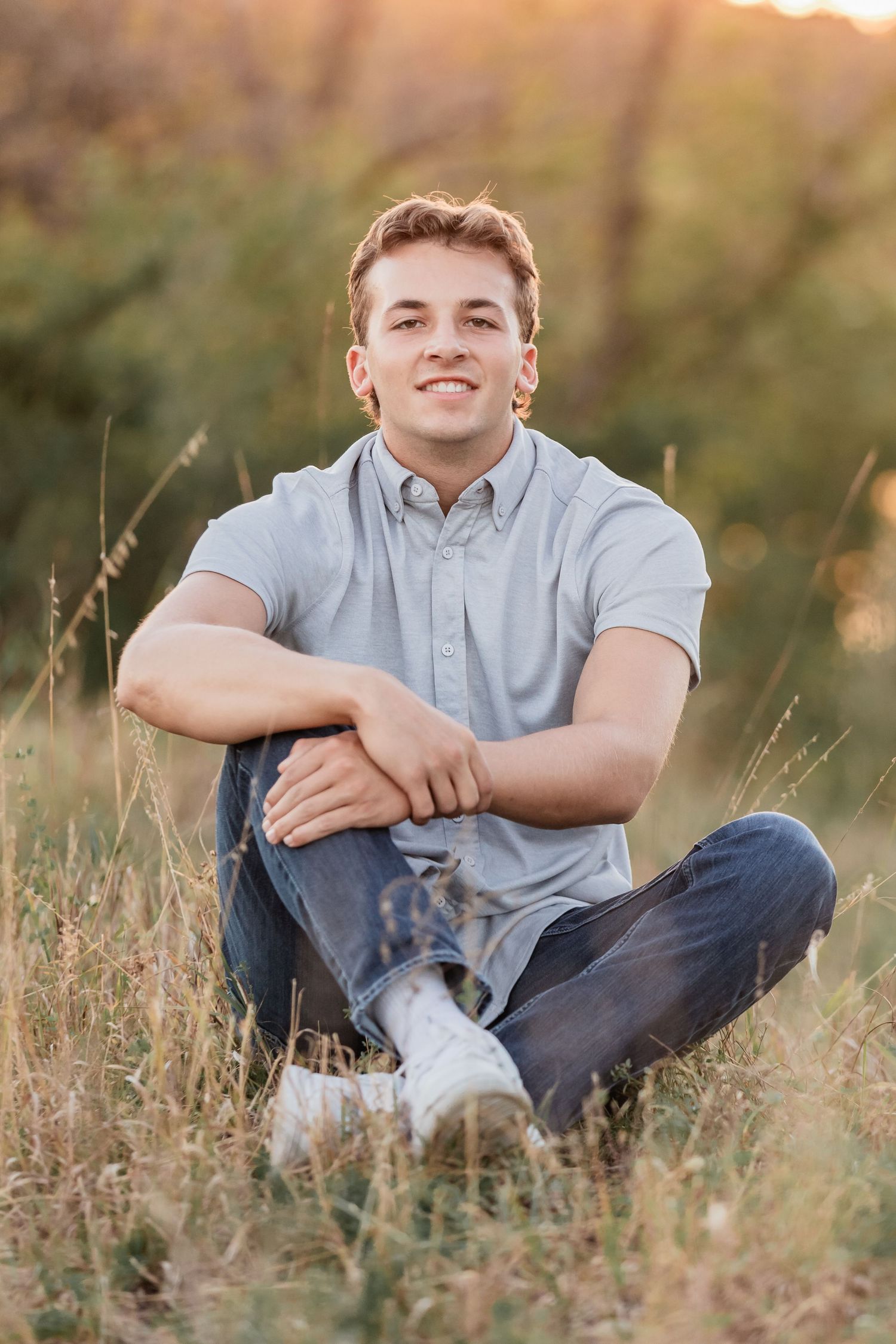 Blake sits in a tall grassy field with his arsm wrapped around his legs