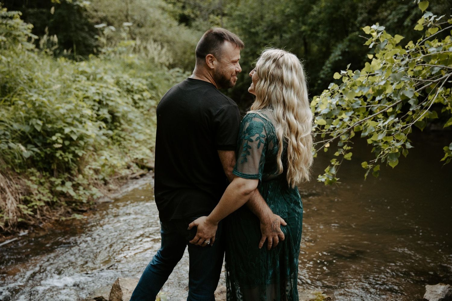 Engaged couple playfully grab each other's butts as they stand in a rushing creek