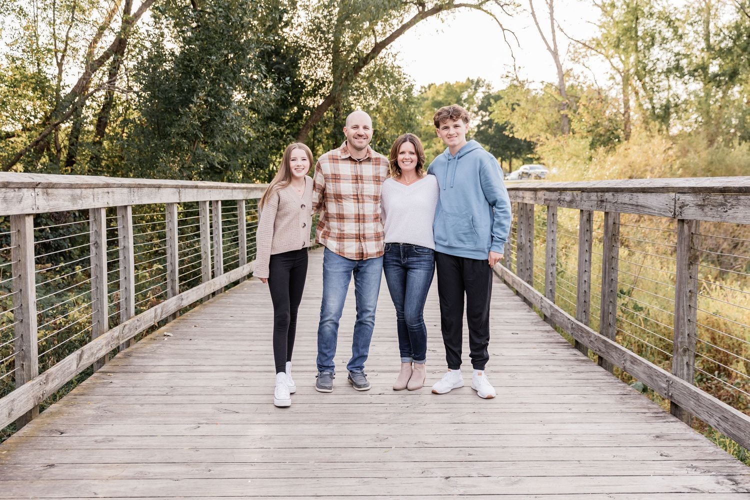 Family with two teenagers give a loose family hug on a wooden footbridge at Lebanon Hills Park in Eagan