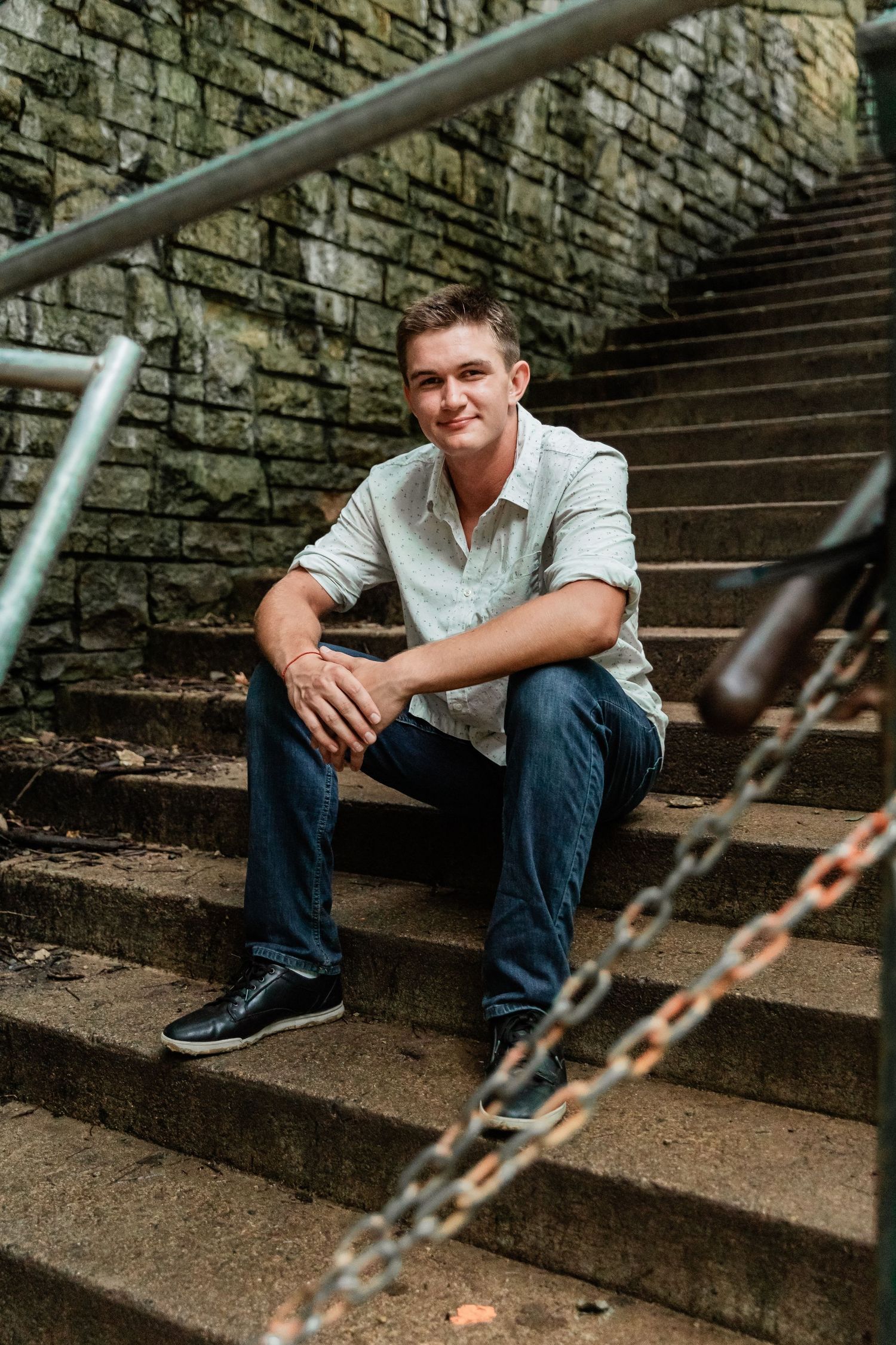 Teenage boy sits on a grungy staircase with his arms resting on his knees for his Minnehah Falls senior photos