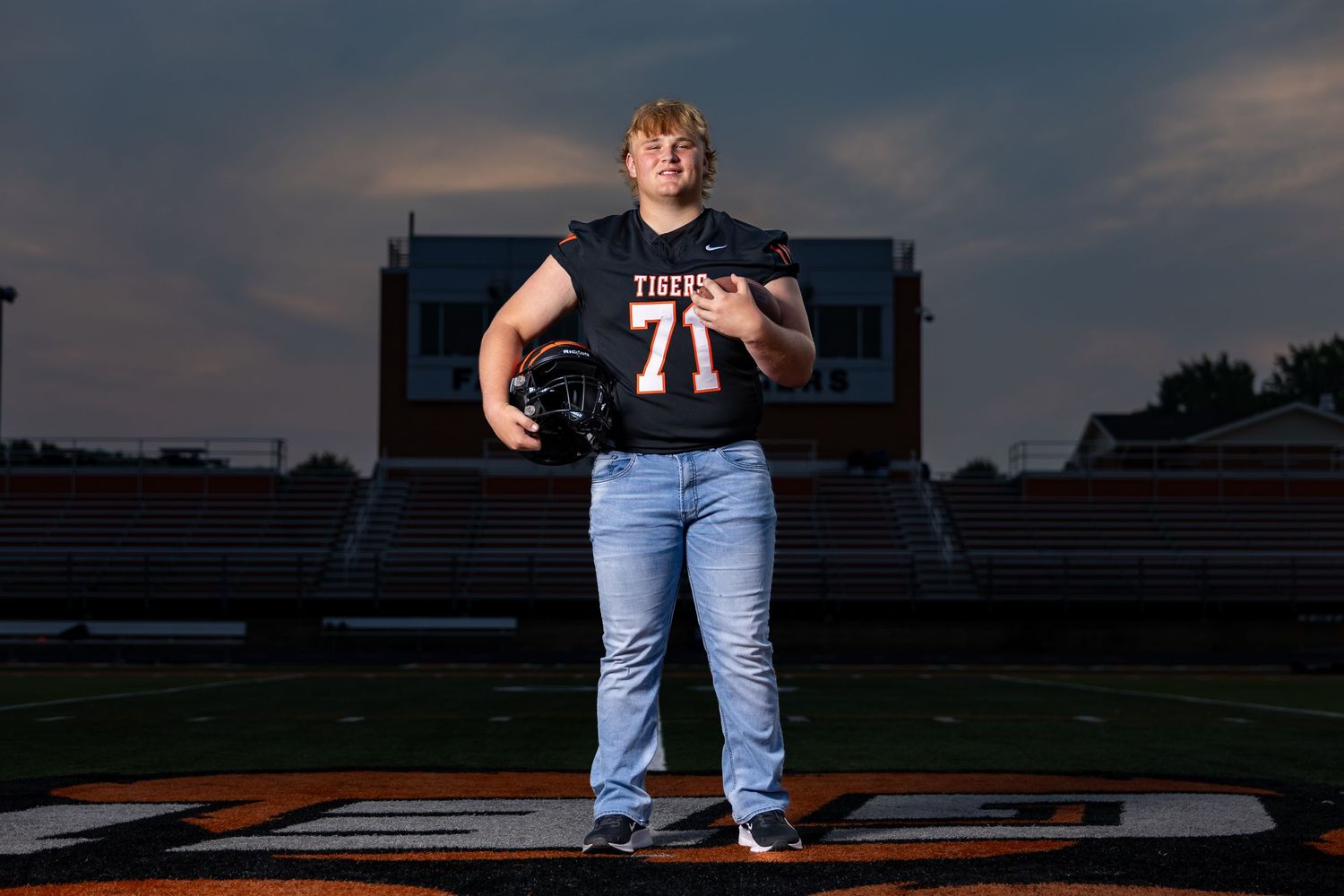 Isaac stands holding football and helmet at center field for Farmington High School