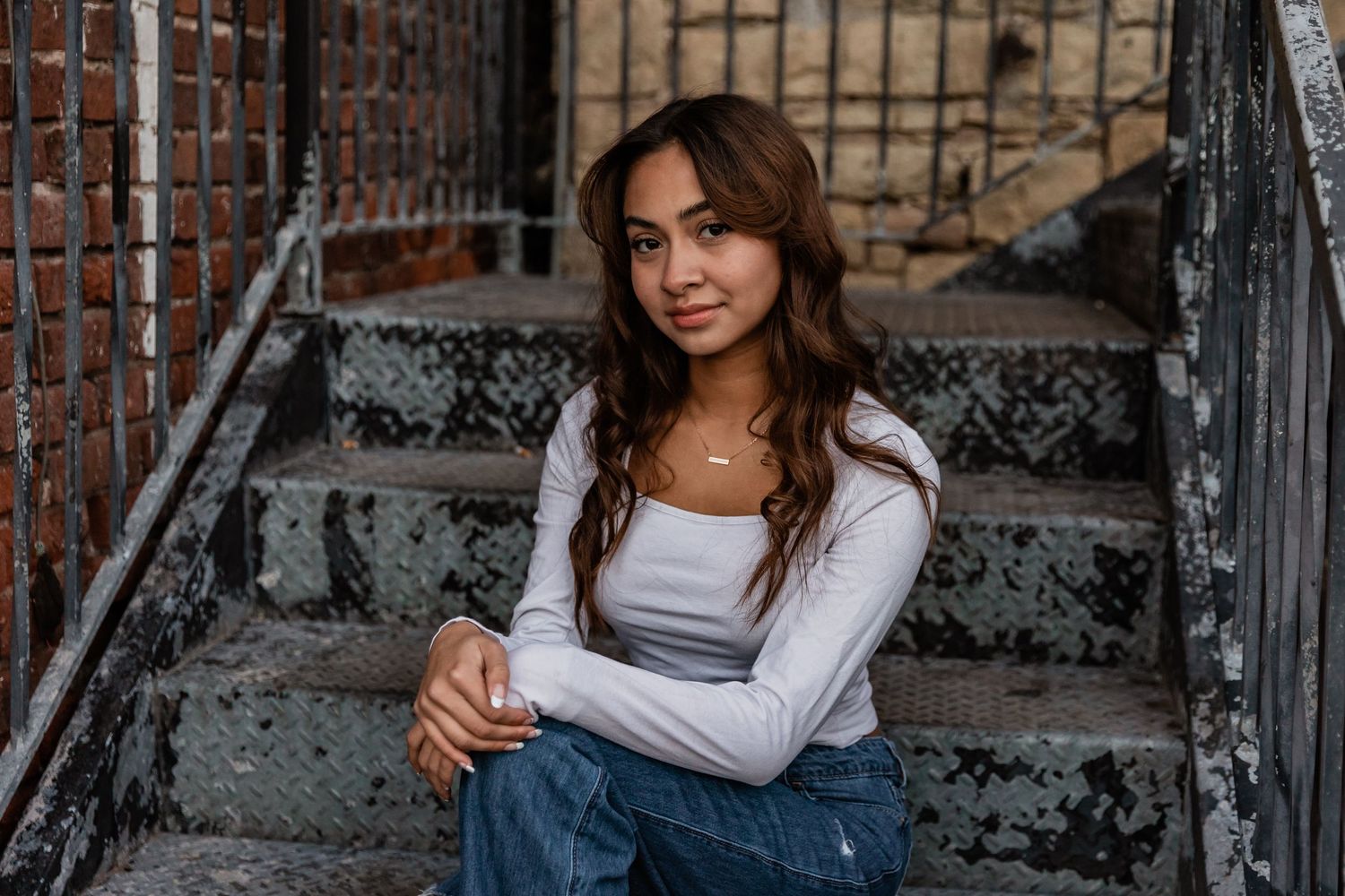 Senior girl sits on worn down metal stairs attached to an old brick building in Stillwater