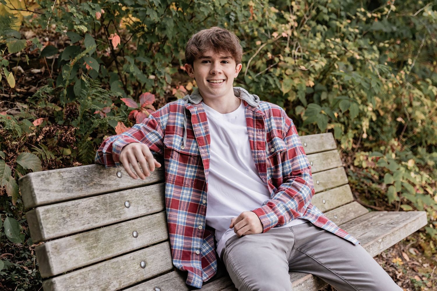 Wade rests his arm on the back of a wooden bench on the wooded trails of Lebanon Hills for his senior photos