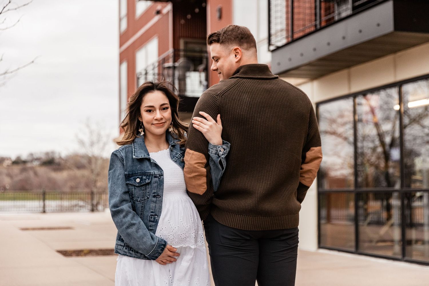 Young pregnant woman wraps her arm around her husband as she holds he baby bump