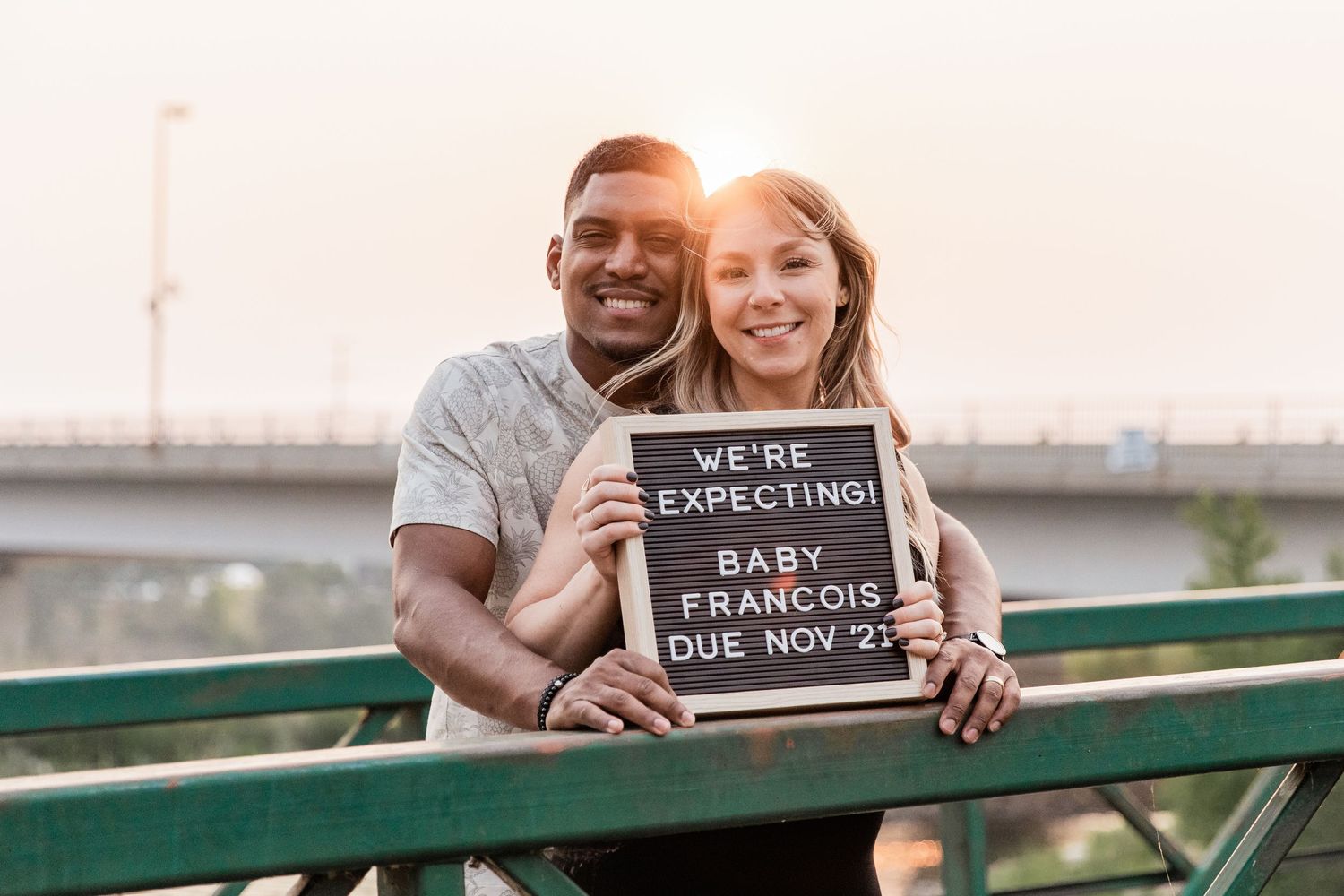 Husband and wife hold a peg board sign announcing their pregnancy and due date