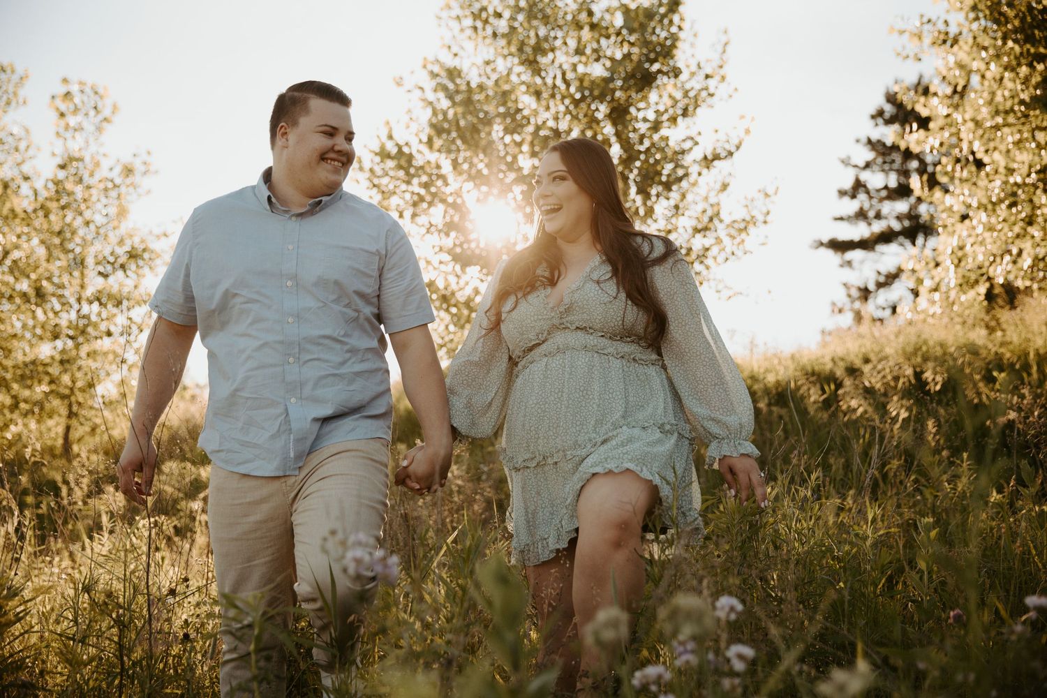 high school sweethearts walk through a field of tall grass at sunset