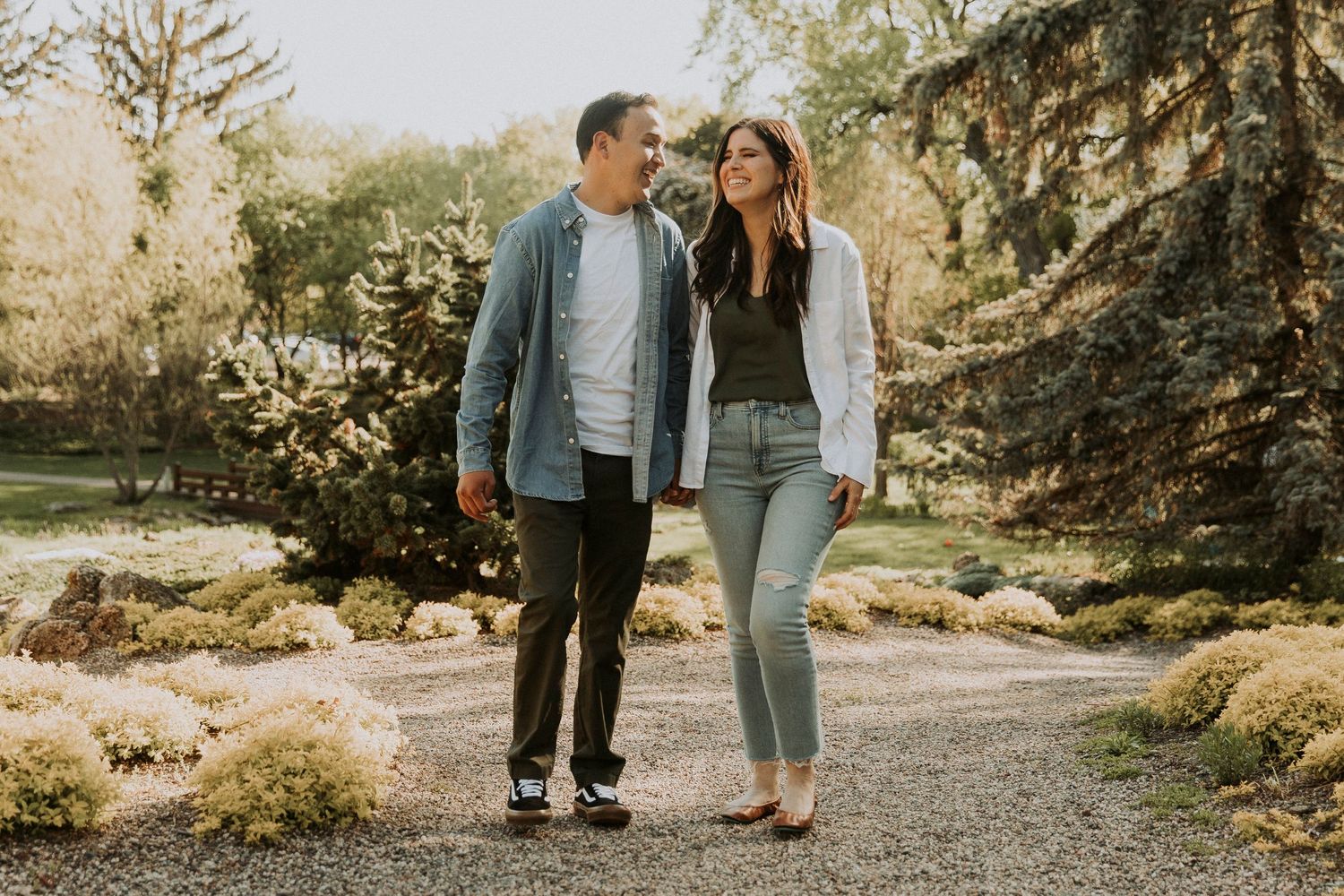 Young woman laughs as her fiance tells her a funny joke walking down a pebble covered path