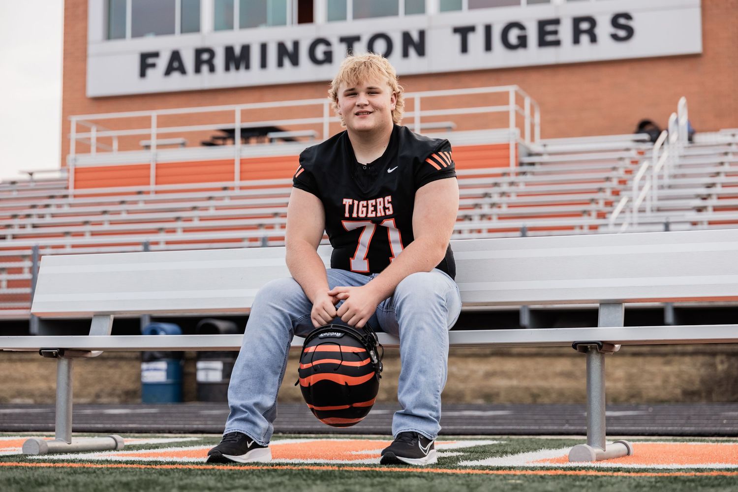 Isaac sits on a metal bench at Farmington Tigers Stadium holding his helmet in his hands