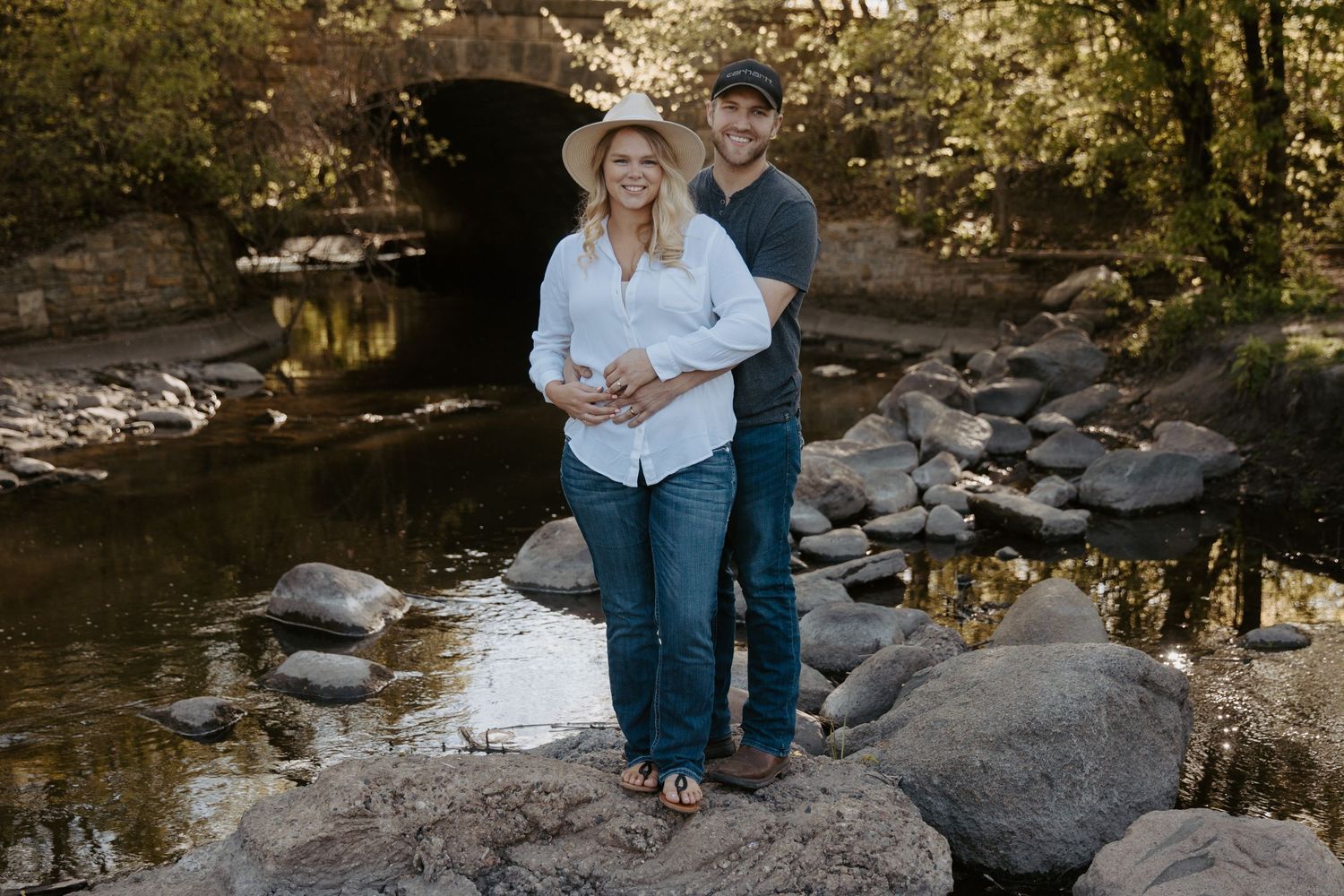 Young man wraps his arms around his fiance standing in a babbling brook