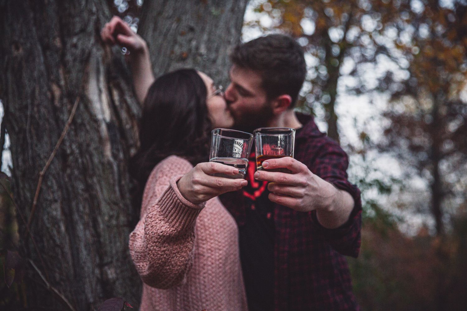 young couple kisses as they tap glasses for engagement photos