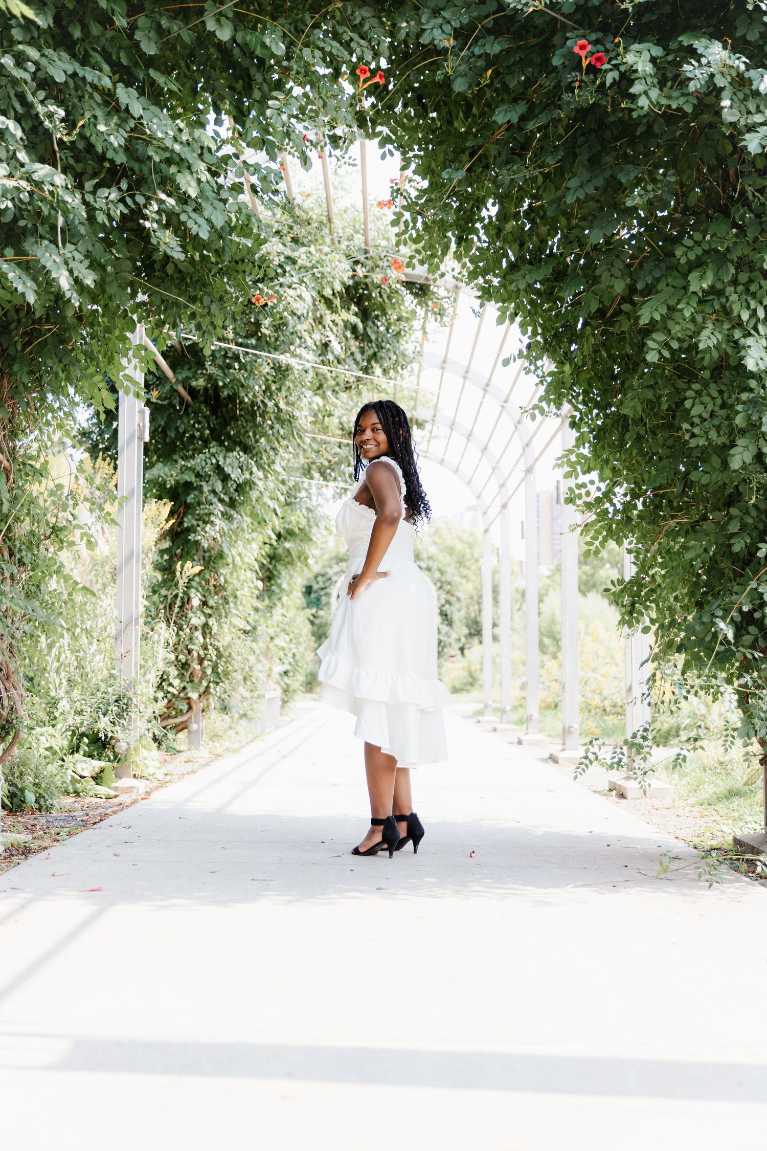 Senior girl looks back over her shoulder as she stands beneath an ivy covered archway on a bright sunny day at Minneapolis Sculpture Garden