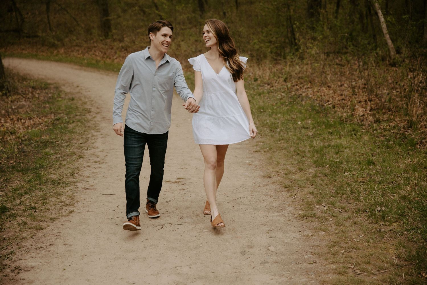 Young couple playfully walks down a dirt path holding hands and laughing together