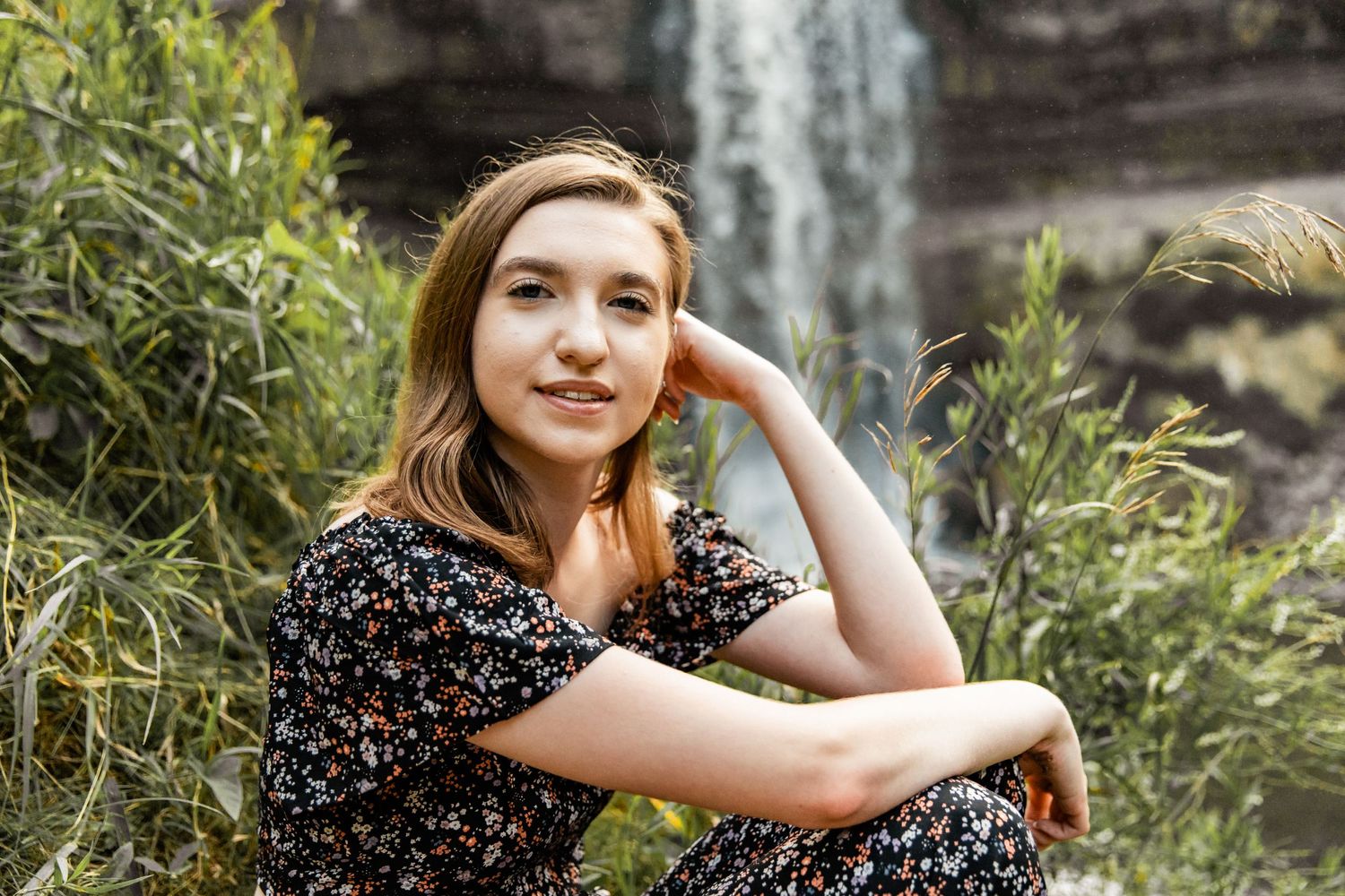 Sydney rests her head on her hand while she sits on a hill with Minnehaha Falls crashing down behind her