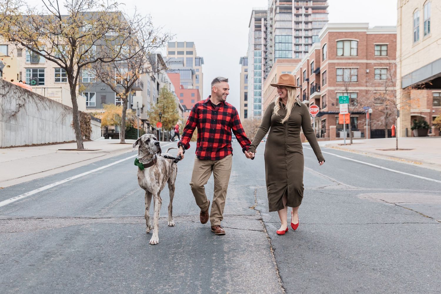 Husband and wife hold hands as they walk their great dane puppy down the middle of an empty street in Minneapolis