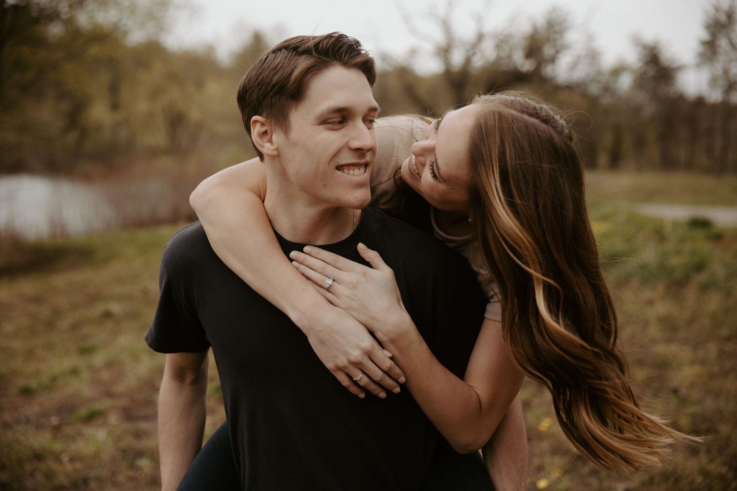 Young woman leans over her fiance's shoulder as they gaze into each other's eyes