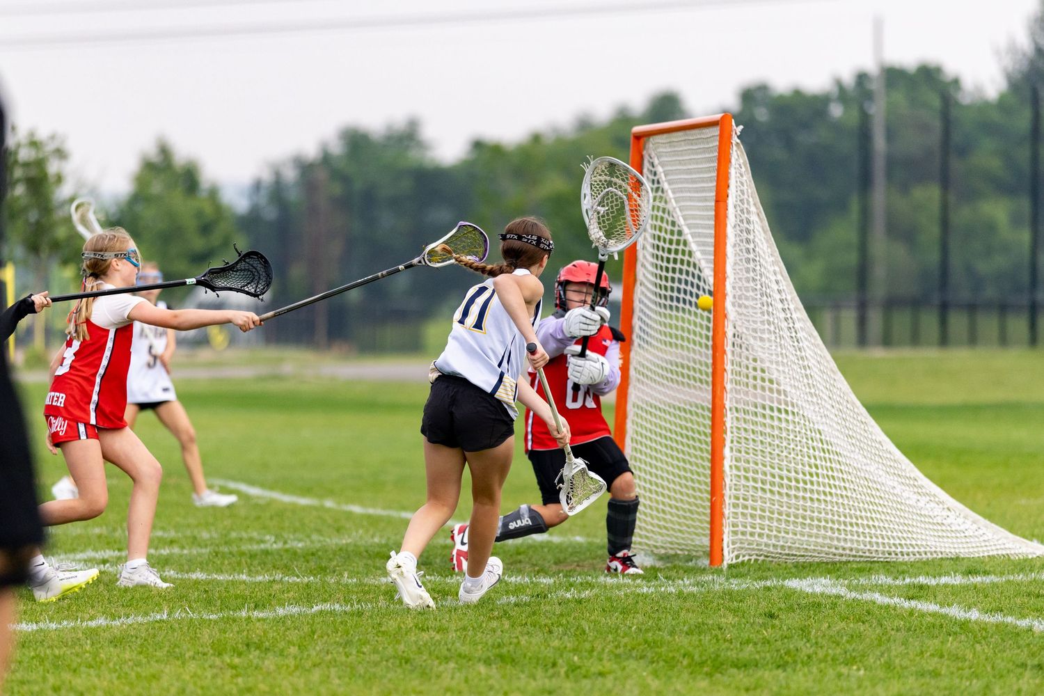 Girls youth lacrosse player scores a goal from the side of the net