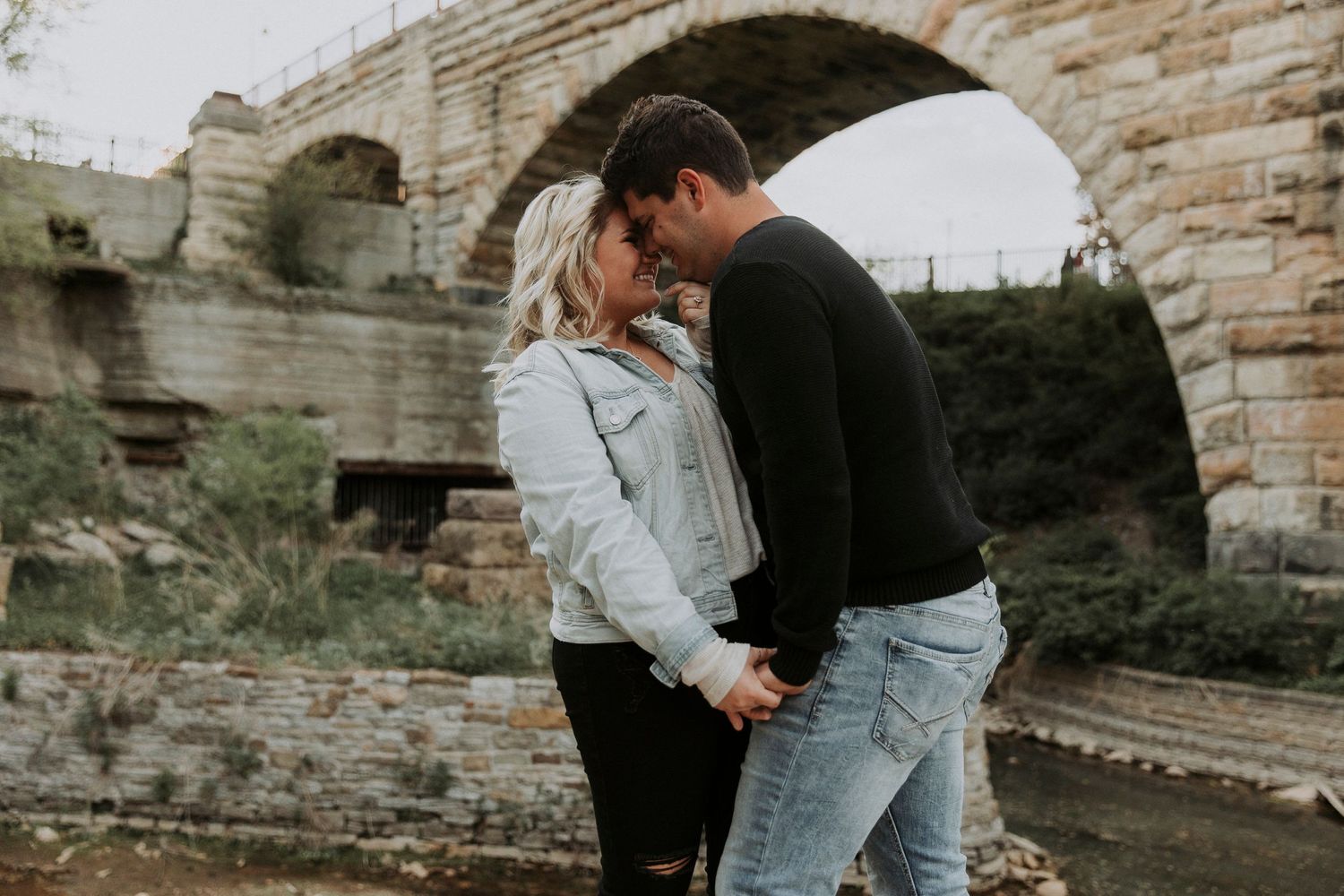 engaged couple embraces each other in front of stone arch bridge