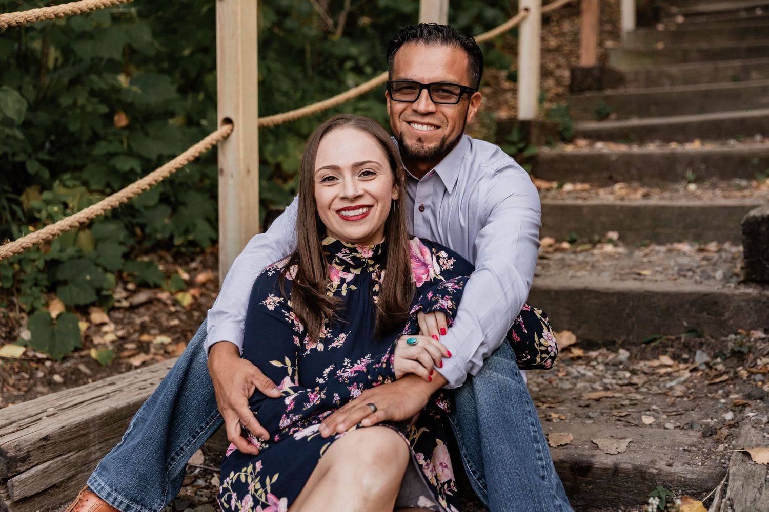 A joyful hispanic couple rest on a rustic wooden staircase in the woods with a golden glow of sunset illuminating the background