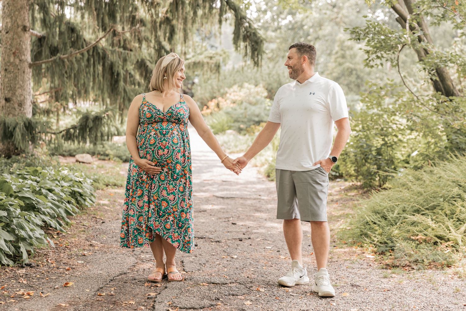 Pregnant couple stand with hands outstretched as they gaze into each other's eyes