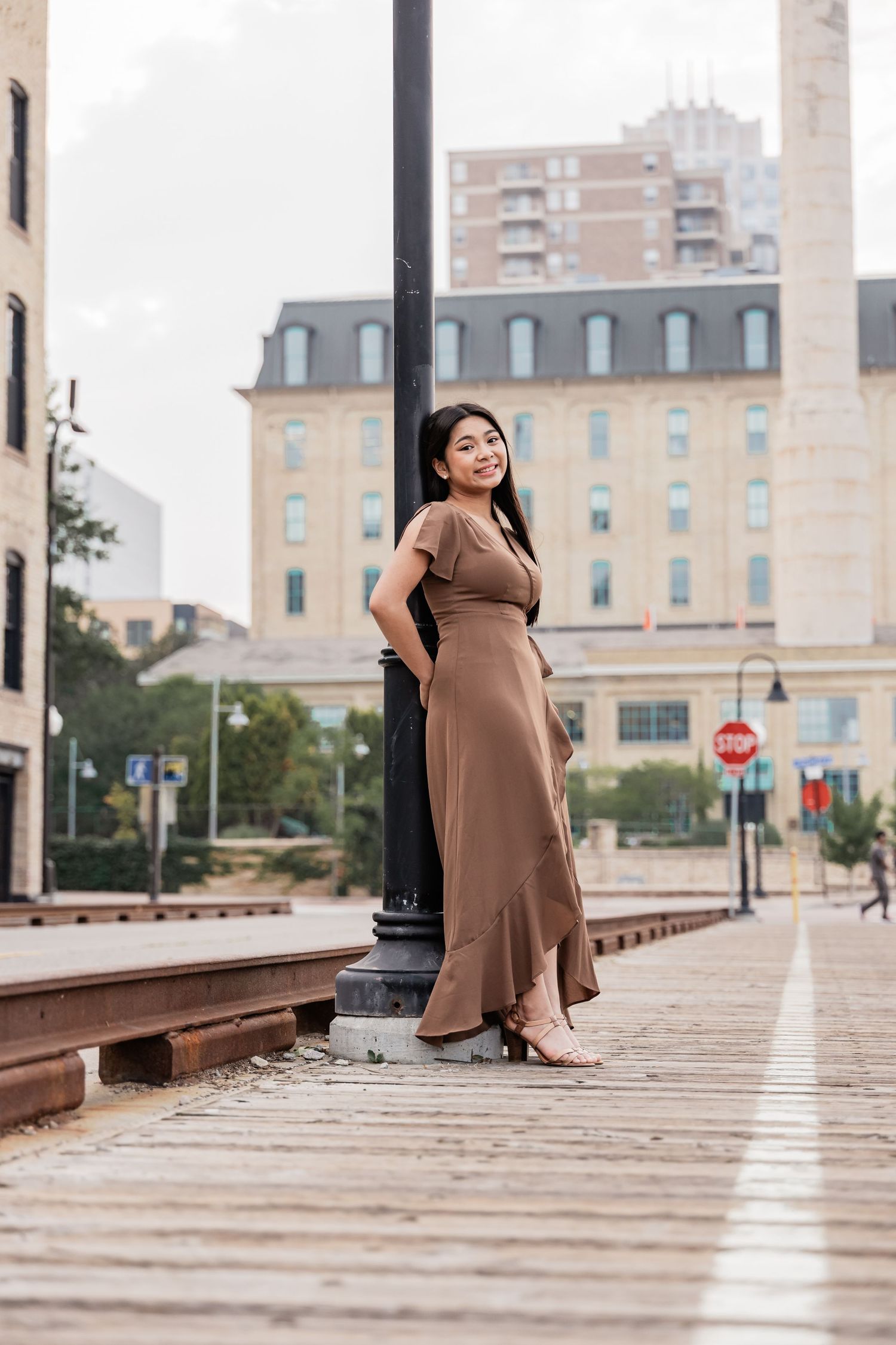 Nina leans into a light post at Mill Ruins Park in Minneapolis with her arms crossed behind her back