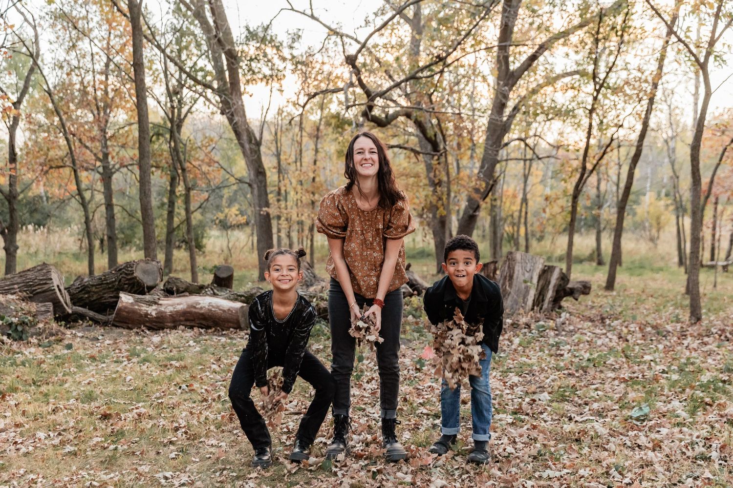 Mom stands between her children as they prepare to throw a handful of leaves into the air