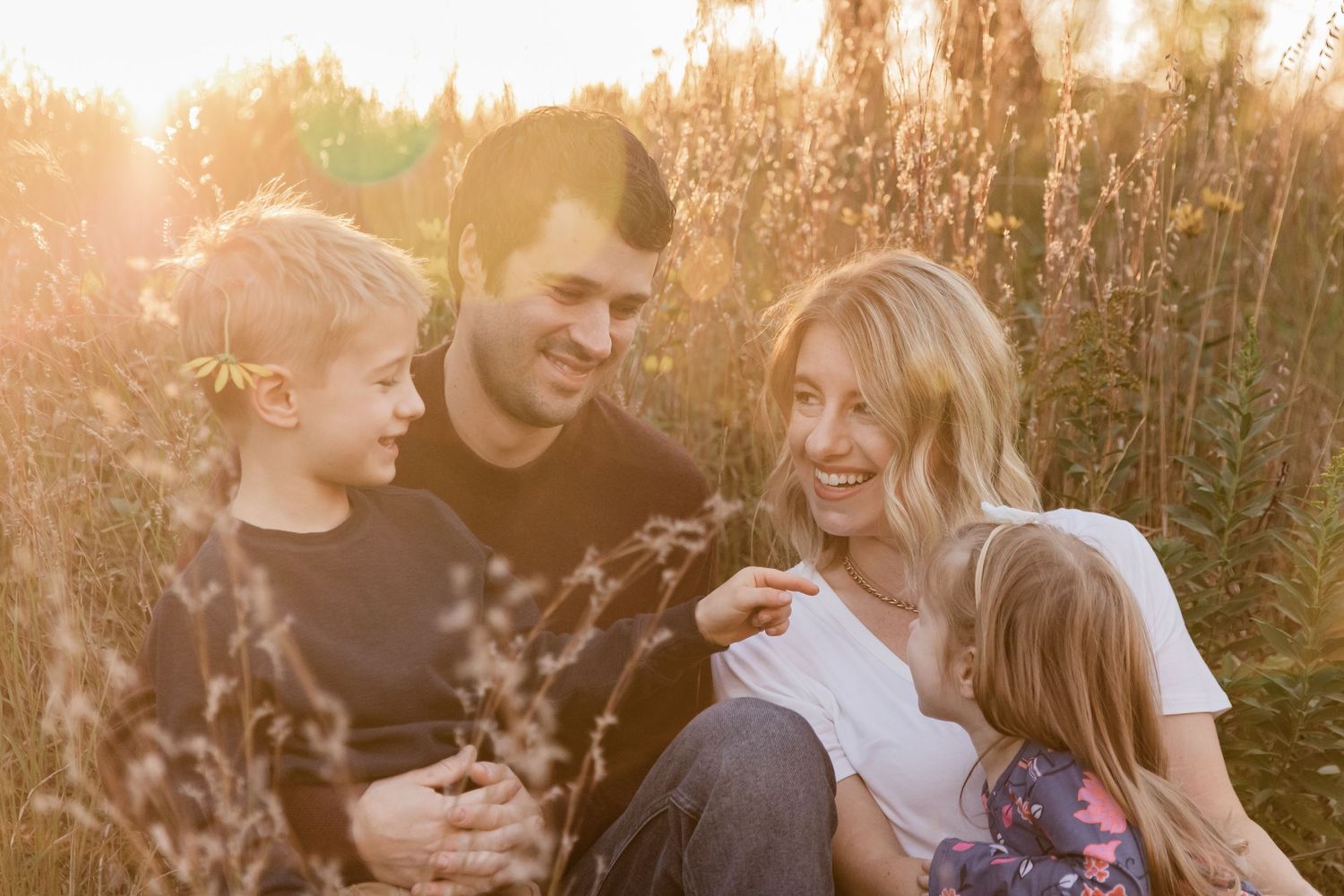 family of four with young children snuggle up in tall grass on a hill during golden hour eden prairie mn riley lake park