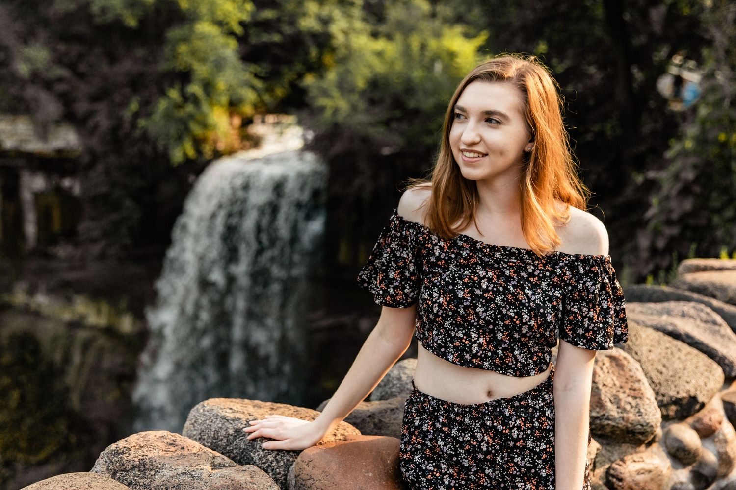 Sydney casually looks off to the side as she stands near a rock wall