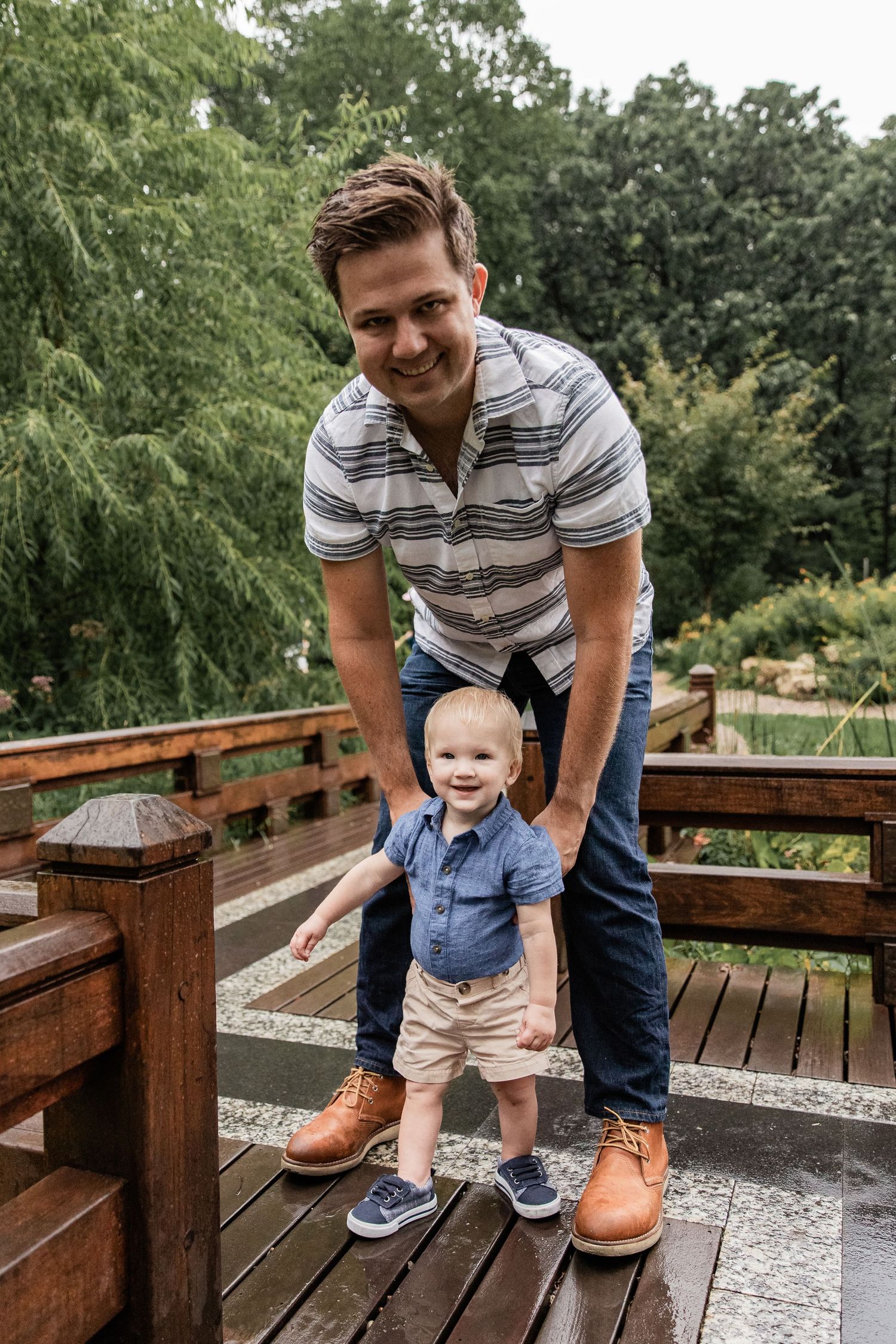 Dad stands on a wet bridge with his baby boy and holds him up to stand