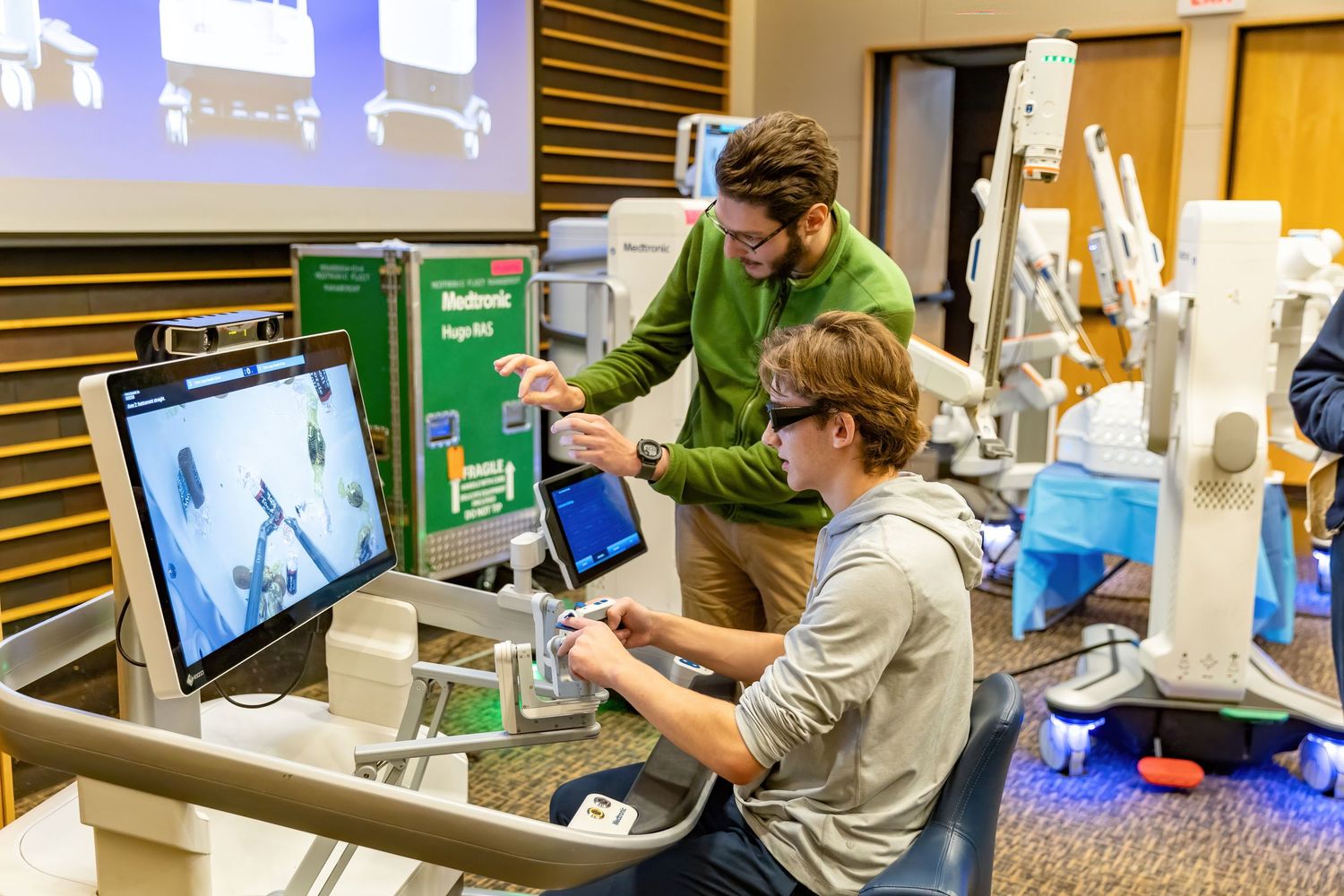 High School student sits at the control console for a surgical robot and plays with the controls