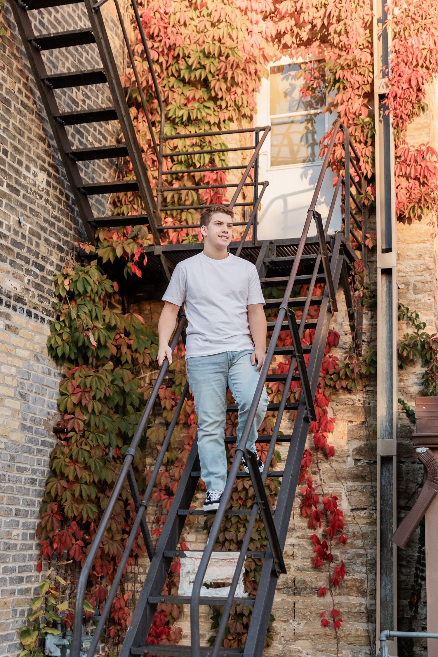 Teen slowly walks down steep staircase hanging off the side of an apartment complex in downtown Northfield for his senior photos