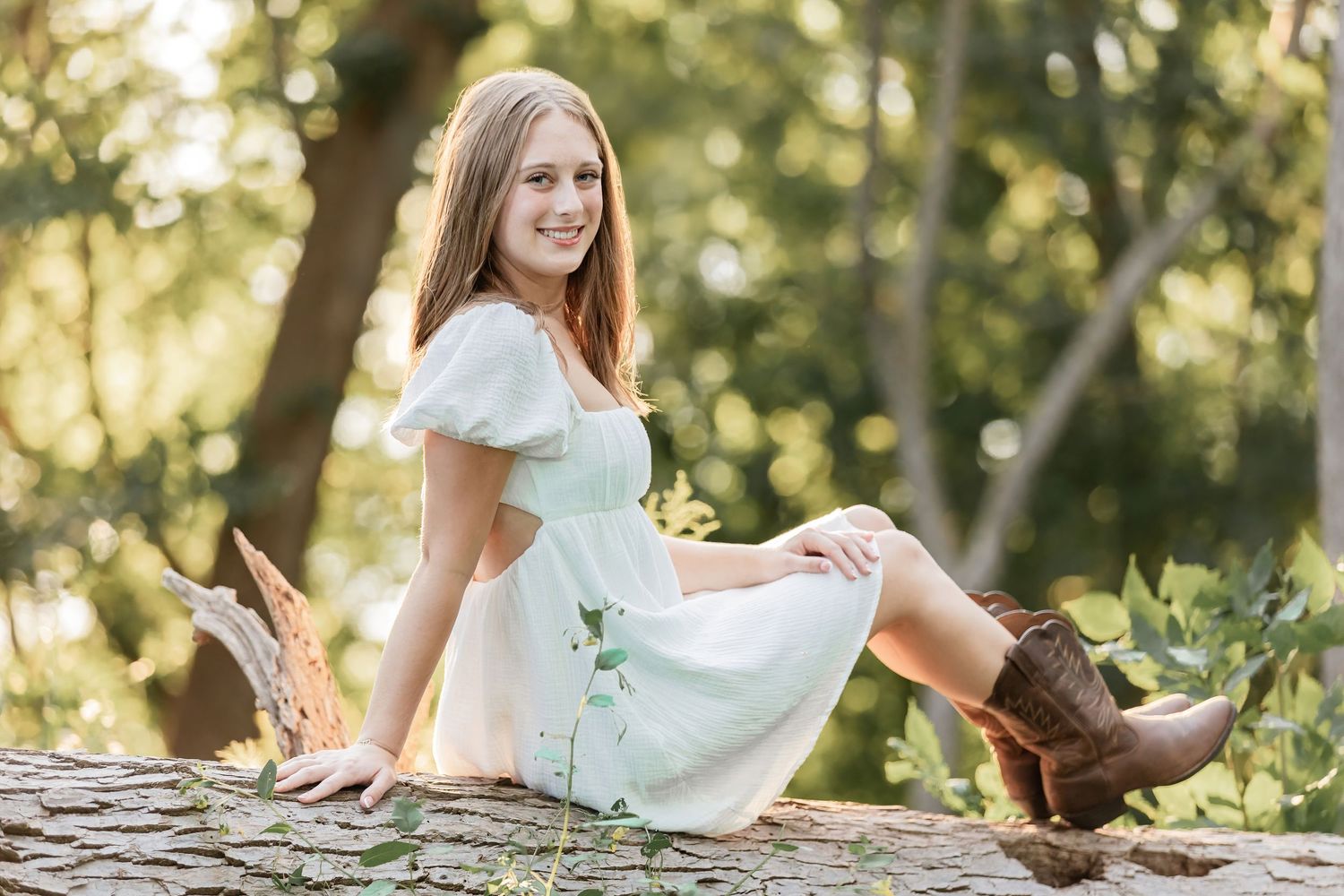 Ella leans back with her legs crossed over each other sitting on a downed tree at Schaar's Bluff in Hastings
