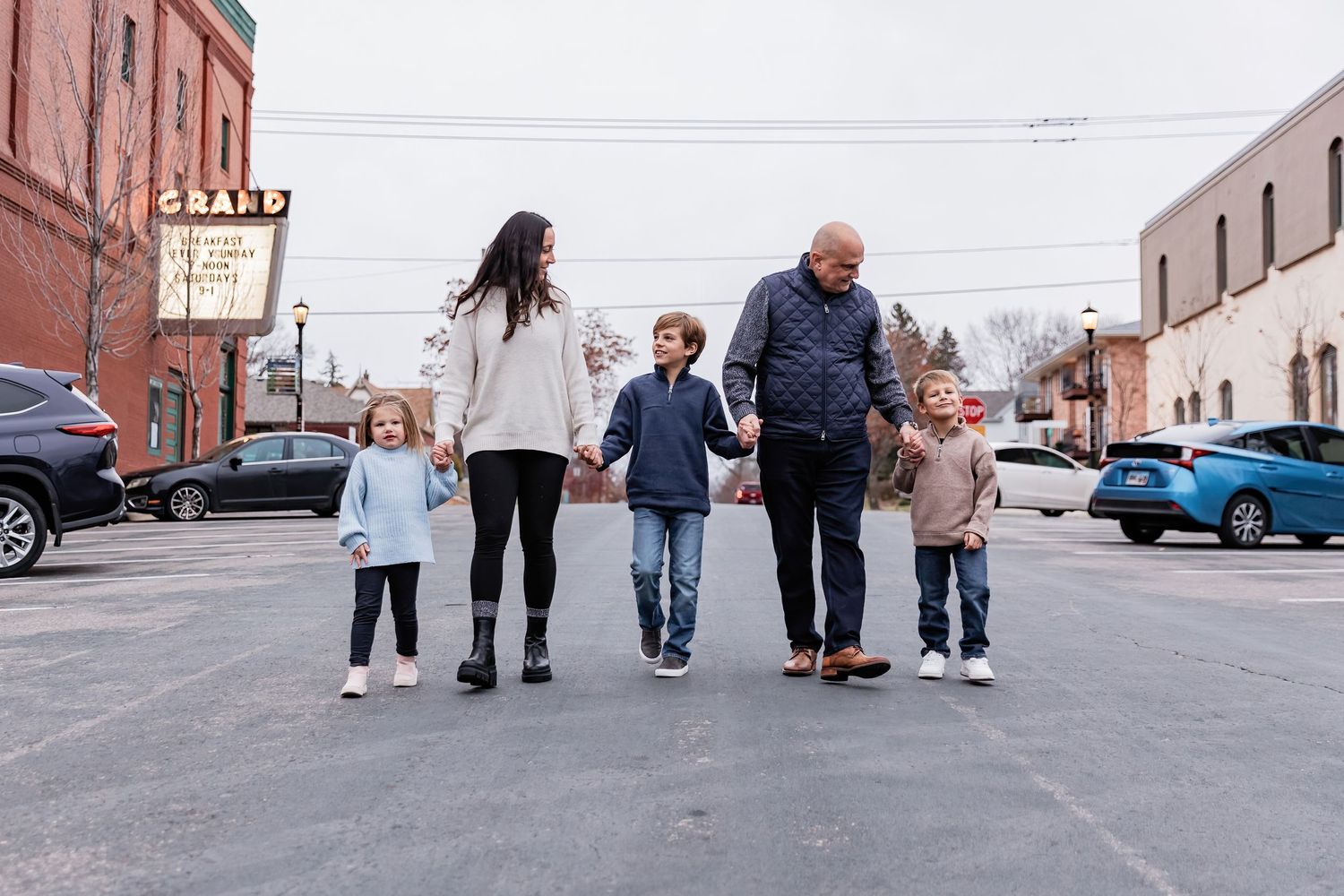Family with three young children holds hands and skip down an empty road in Northfield