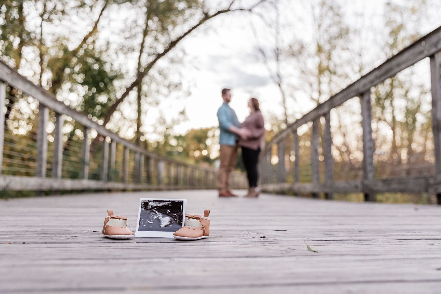 A small pair of booties and an ultrasound printout stand out as the pregnant couple hug and kiss each other in the background