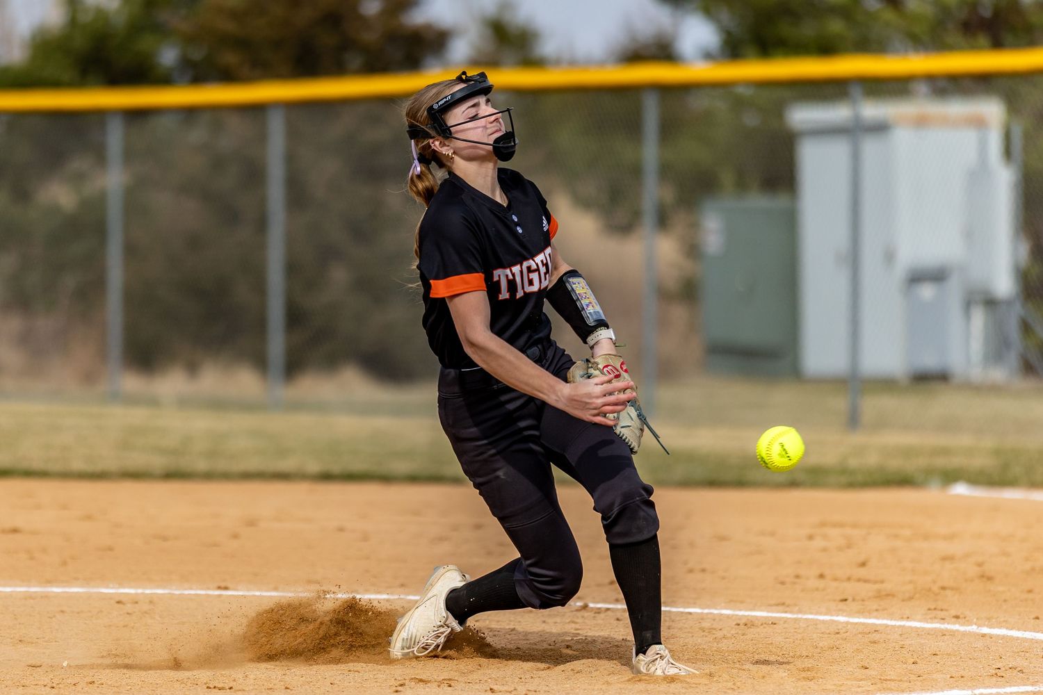 Farmington Tigers softball pitcher kicks up dirt as she tosses a pitch down the middle