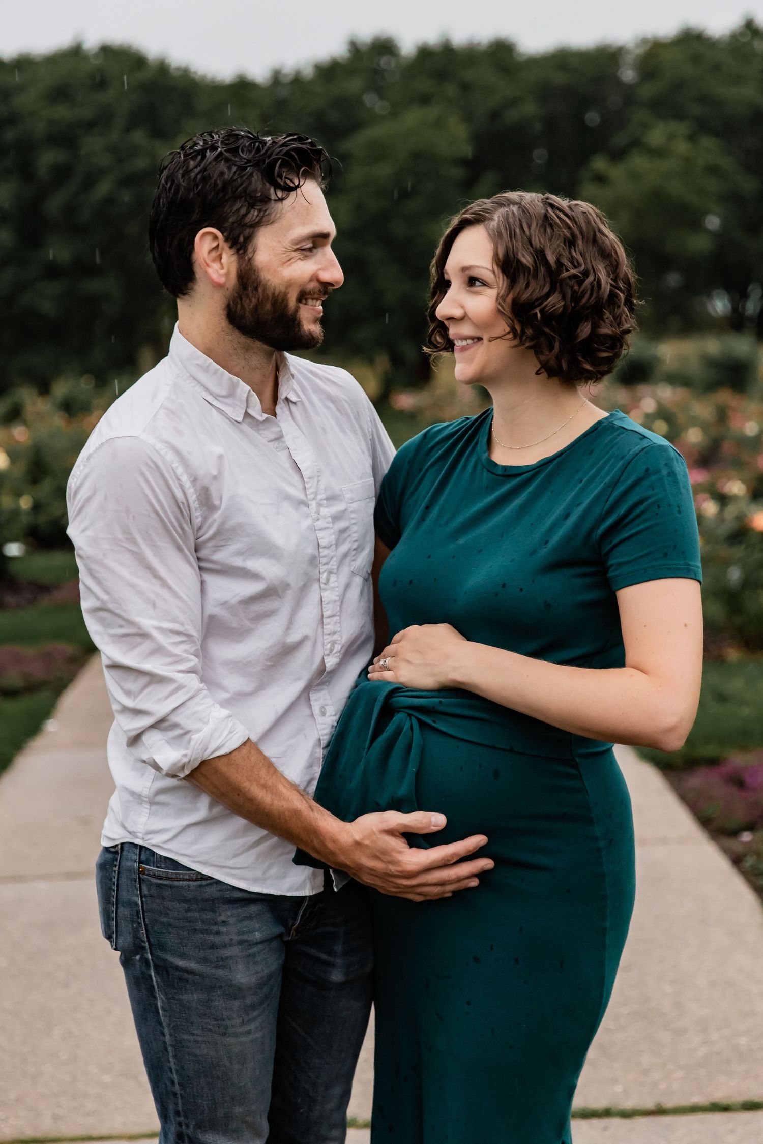Husband rests his hand on his wife's baby bump as they smile at each other