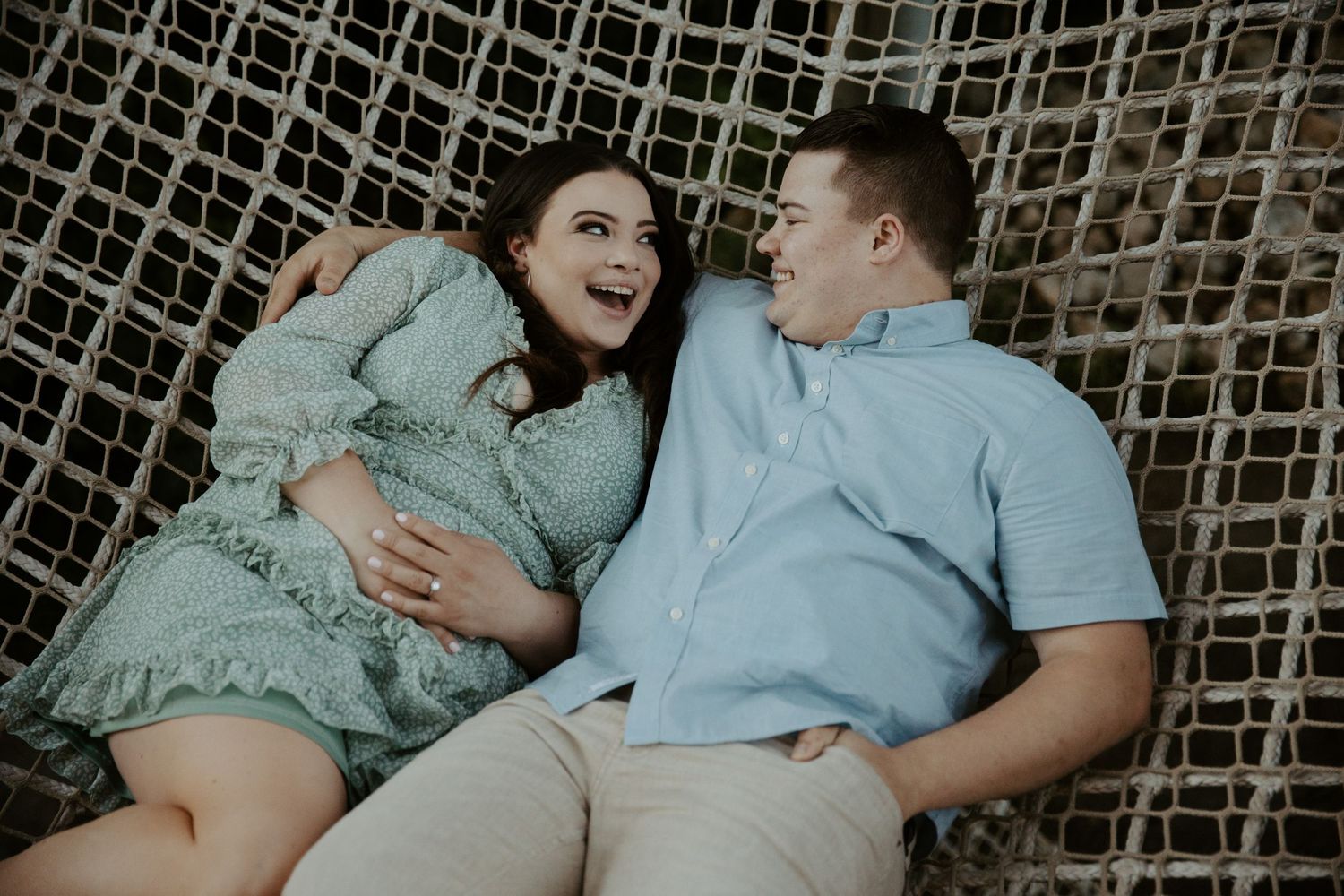 engaged couple cuddles up on a rope canopy