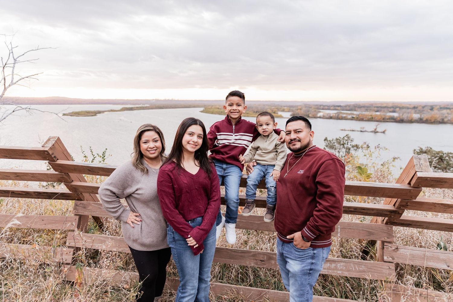 Archila family stands in front of a rustic wooden fence with the sunset shining on the Mississippi River valley beneath them